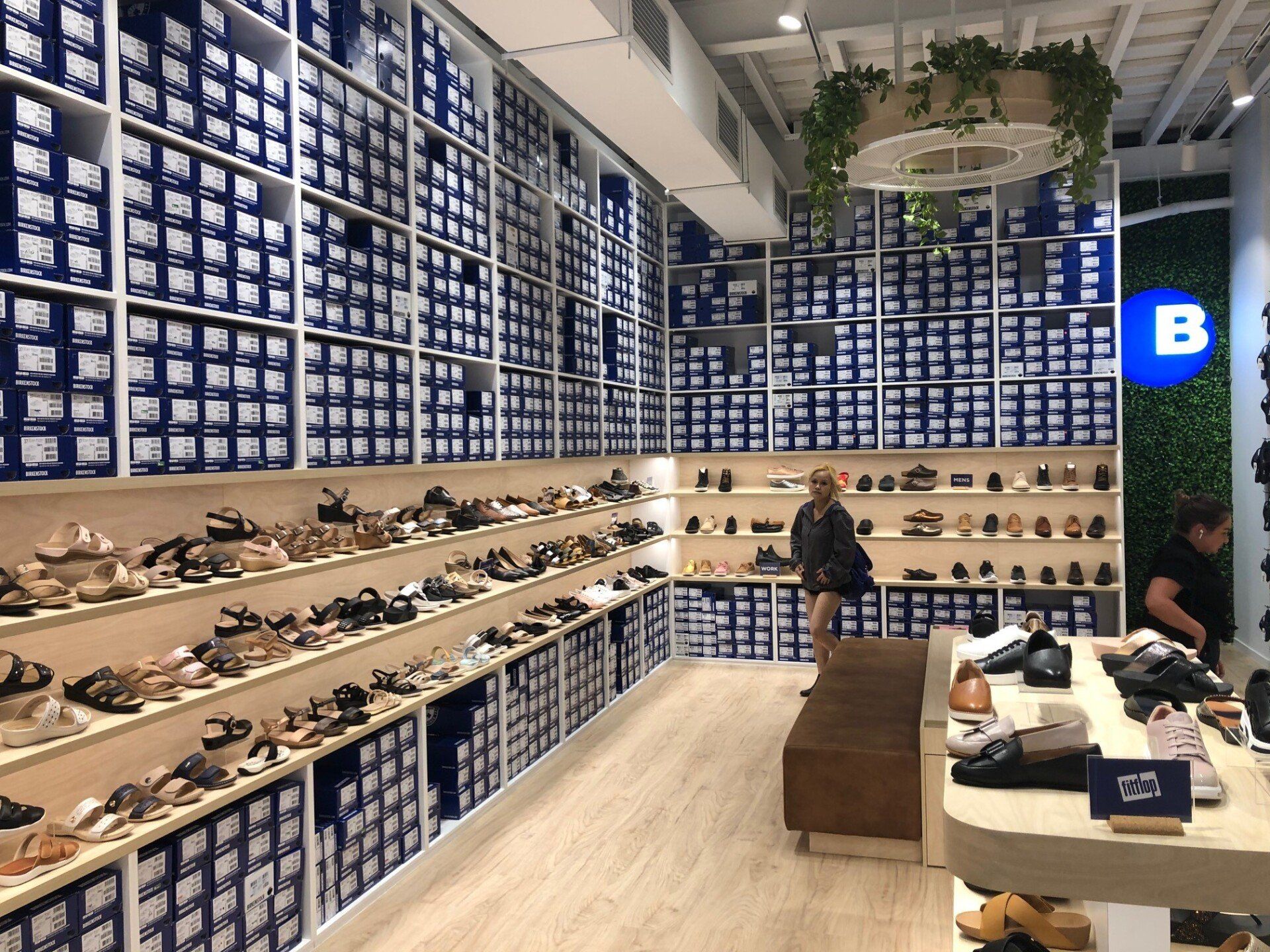 Birkenstock shoe store interior with footwear displays, stacked shoe boxes, customer seating and shoppers browsing products.