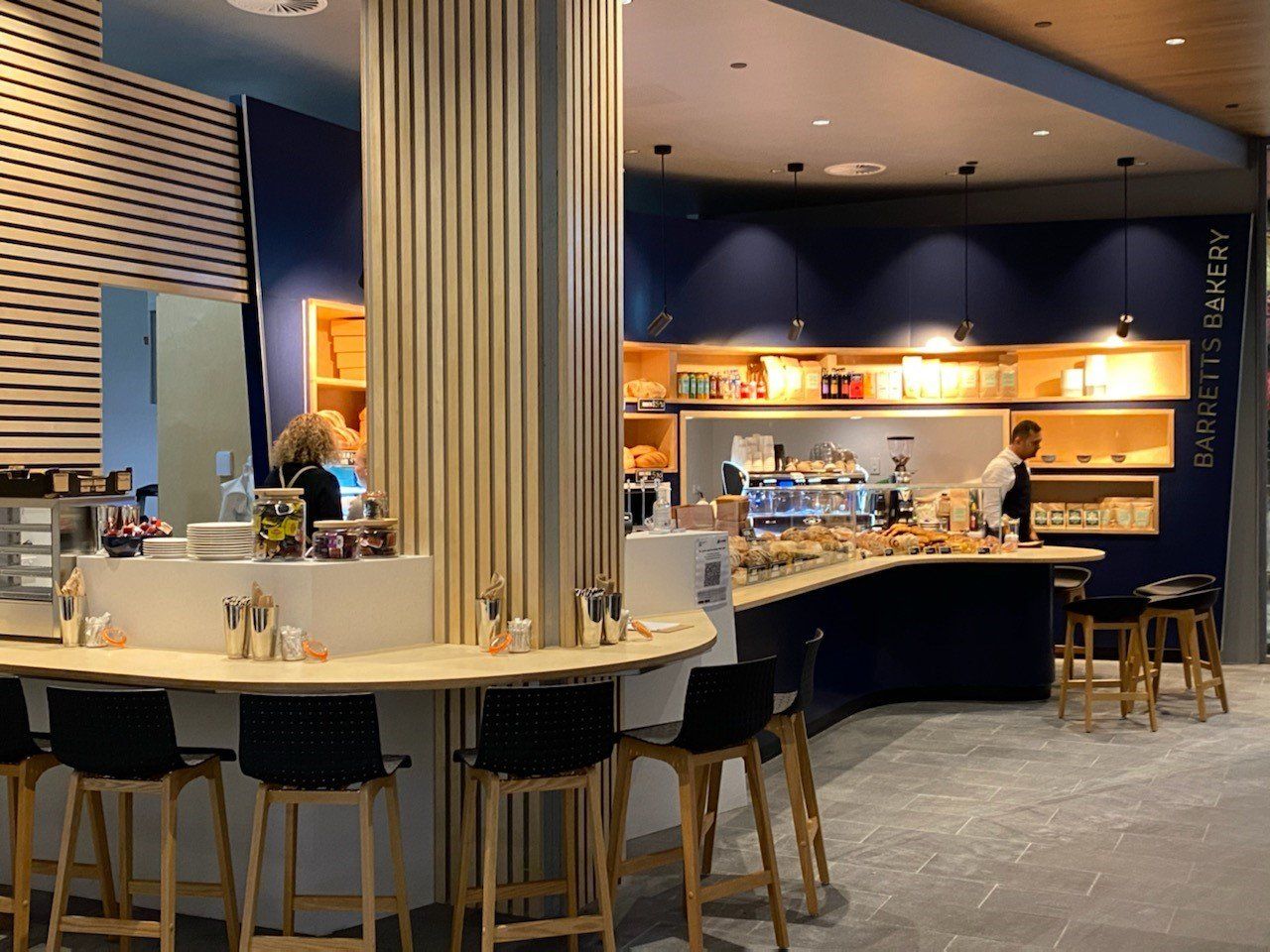 Barretts Bakery seating area with bar stools, coffee service counter and bakery display featuring fresh bread and pastries.
