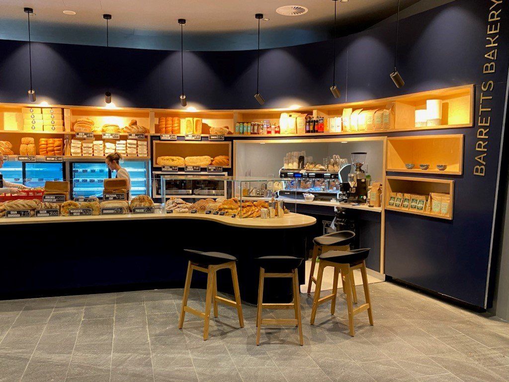 Barretts Bakery counter displaying fresh bread, pastries and baked goods with seating and coffee service area inside the bakery.
