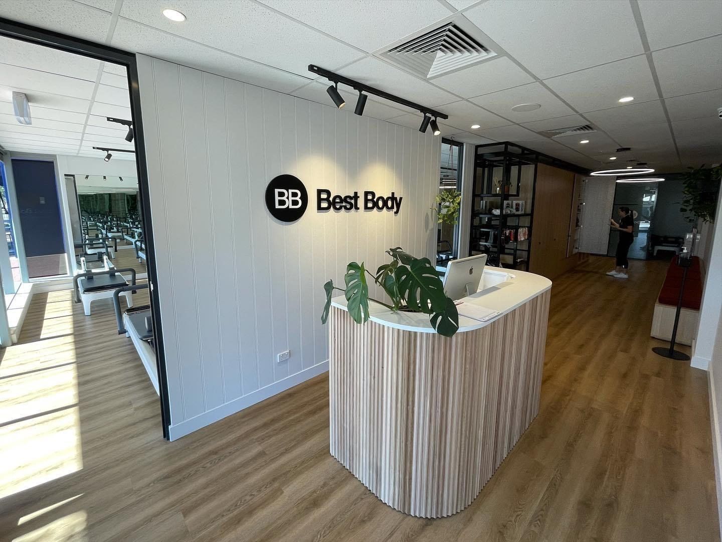 Best Body fitness studio reception area with a curved reception desk, branded wall signage and reformer Pilates equipment visible in the adjoining room.