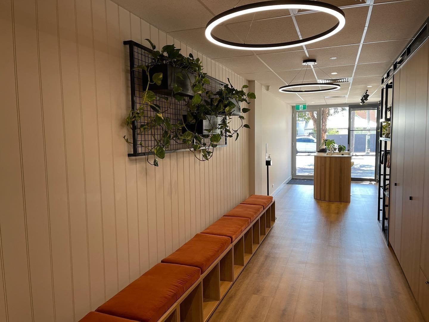 Fitness studio hallway with bench seating, storage cubbies, indoor plants and circular ceiling lights leading to the reception area.