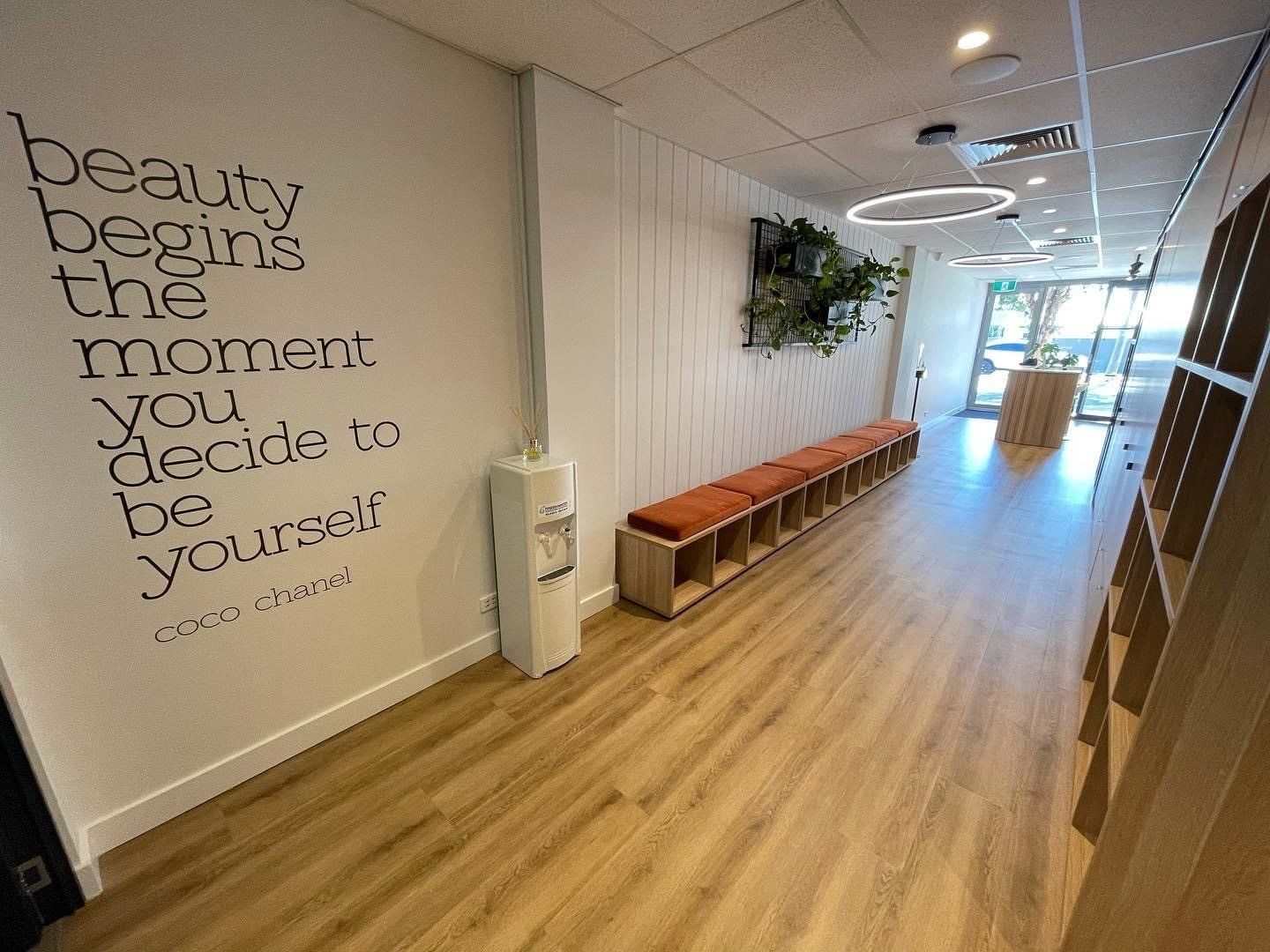 Fitness studio hallway with bench seating, storage cubbies, indoor plants and motivational wall lettering leading to the reception area.