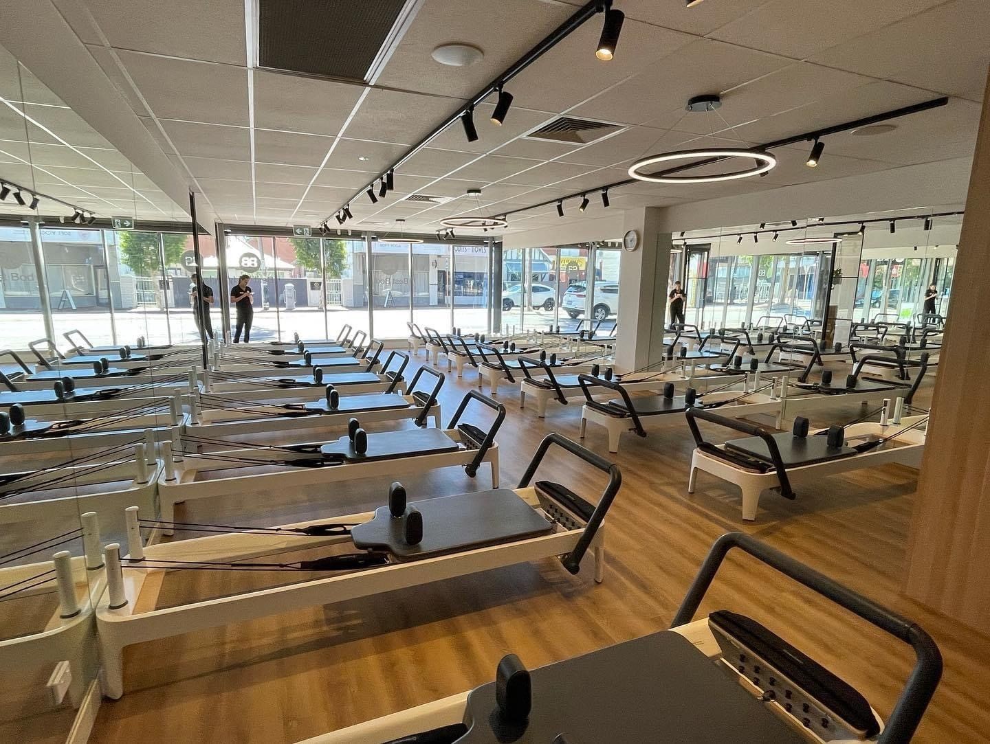 Pilates studio with multiple reformer machines, mirrored walls and large windows allowing natural light into the fitness space.