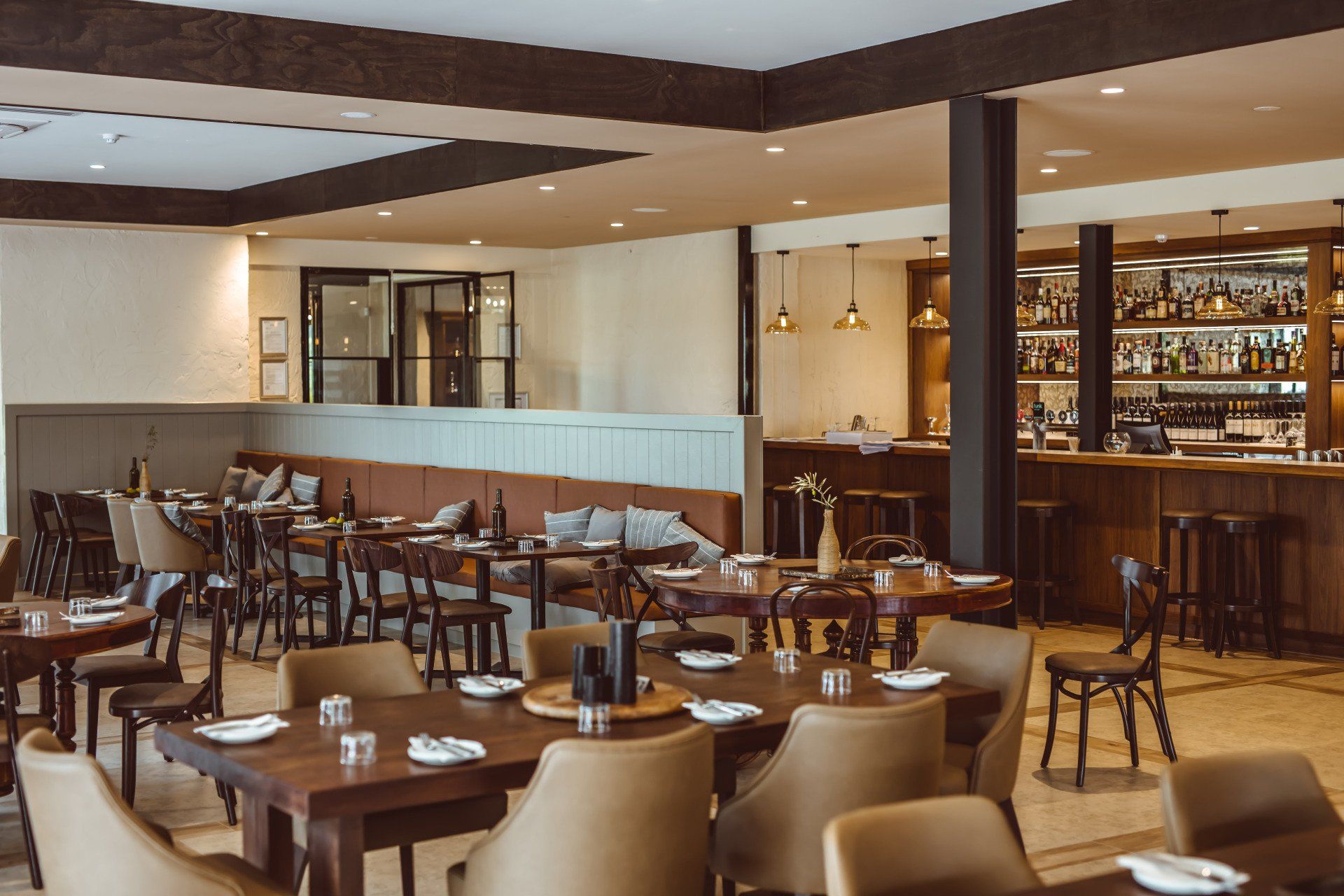 Restaurant dining area with timber tables, upholstered booth seating and a fully stocked bar in the background.