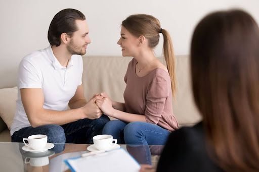A man and a woman are sitting on a couch holding hands.