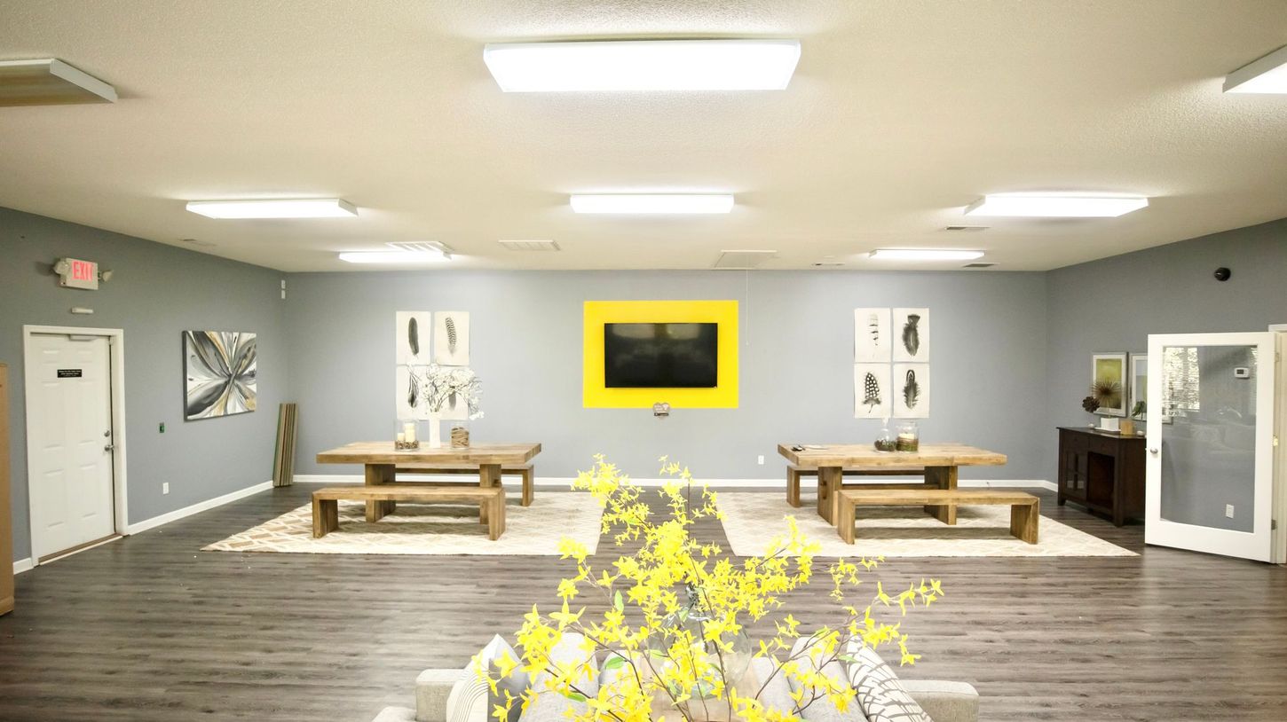 A large room with tables and benches and a television on the wall.