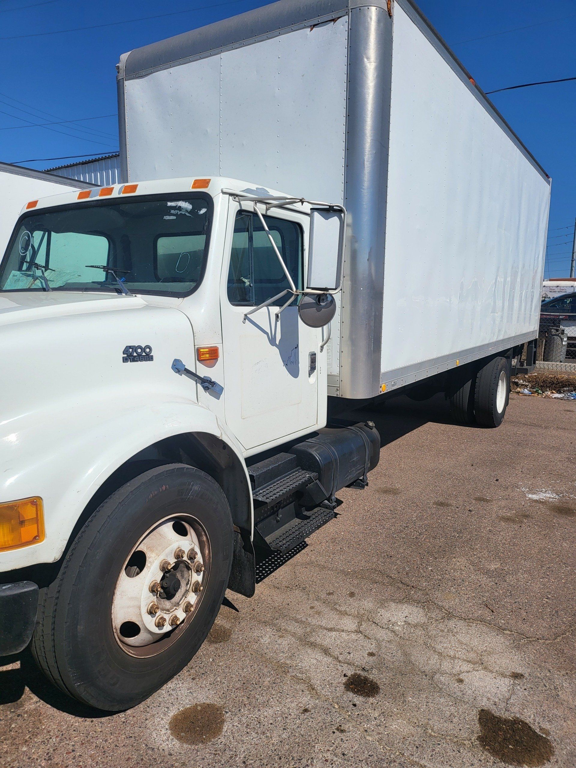 A white box truck is parked in a dirt lot.