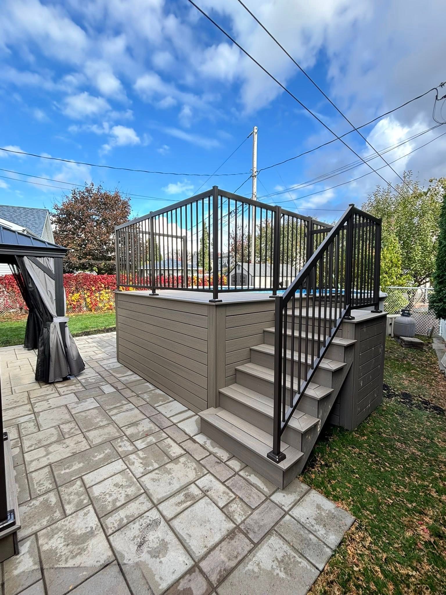 Une terrasse surélevée en composite avec escalier et rambarde en métal noir, aménagée dans un jardin.