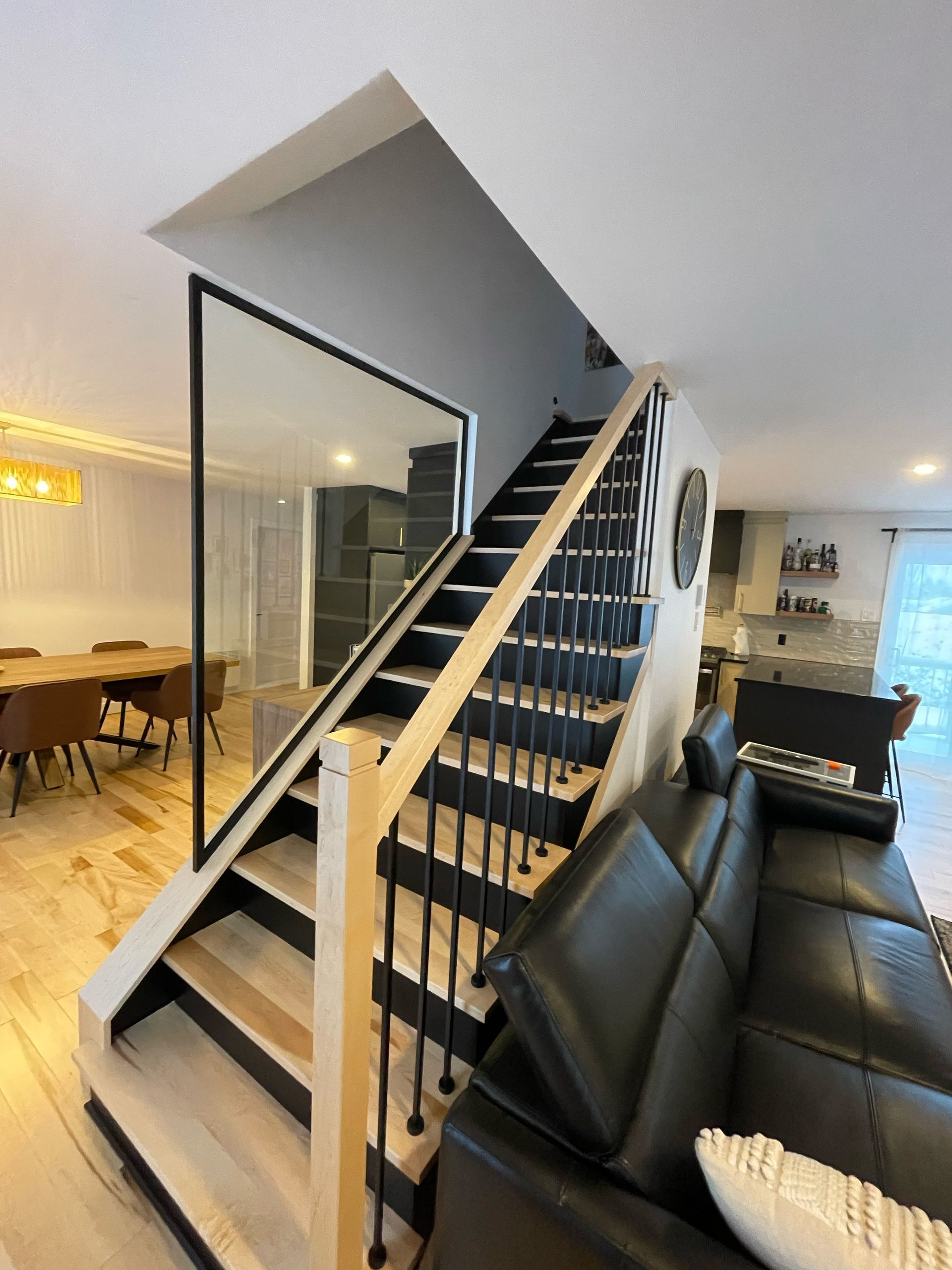 Escalier moderne avec contremarches noires, marches et rampe en bois, et panneau de verre.