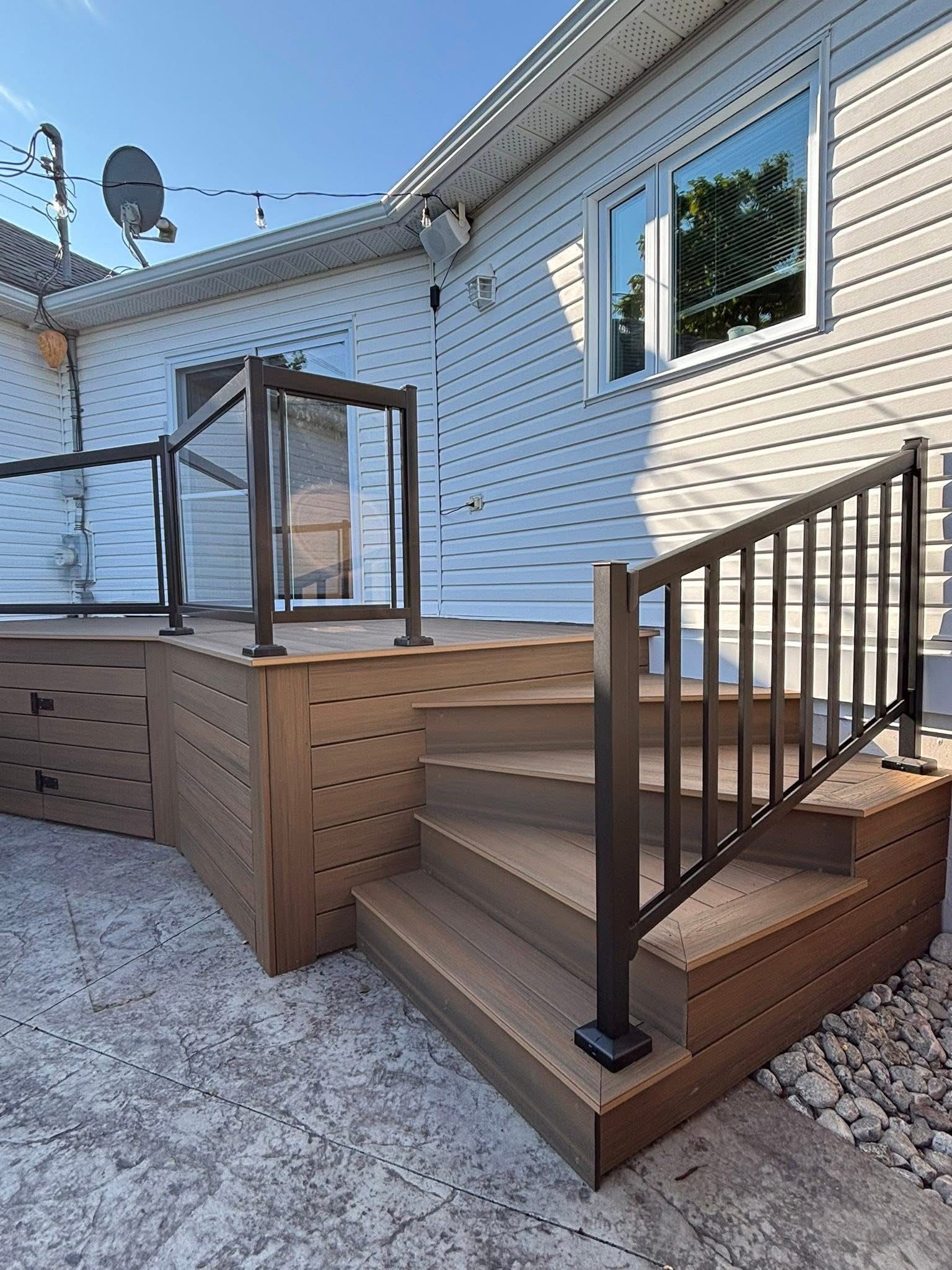 Terrasse composite avec escalier et rambarde noire, adossée à une maison à bardage blanc.