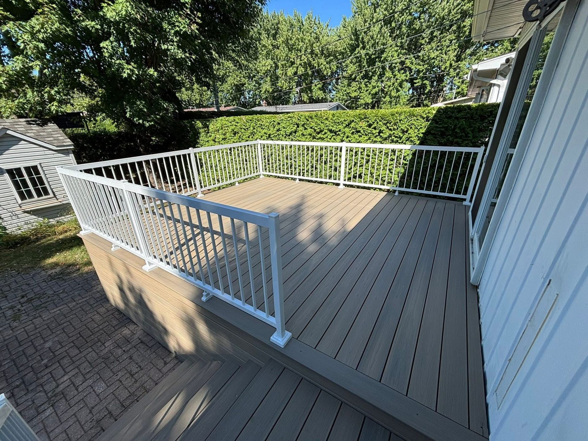 Une terrasse en composite avec des rambardes blanches, des marches et une vue sur les arbres.