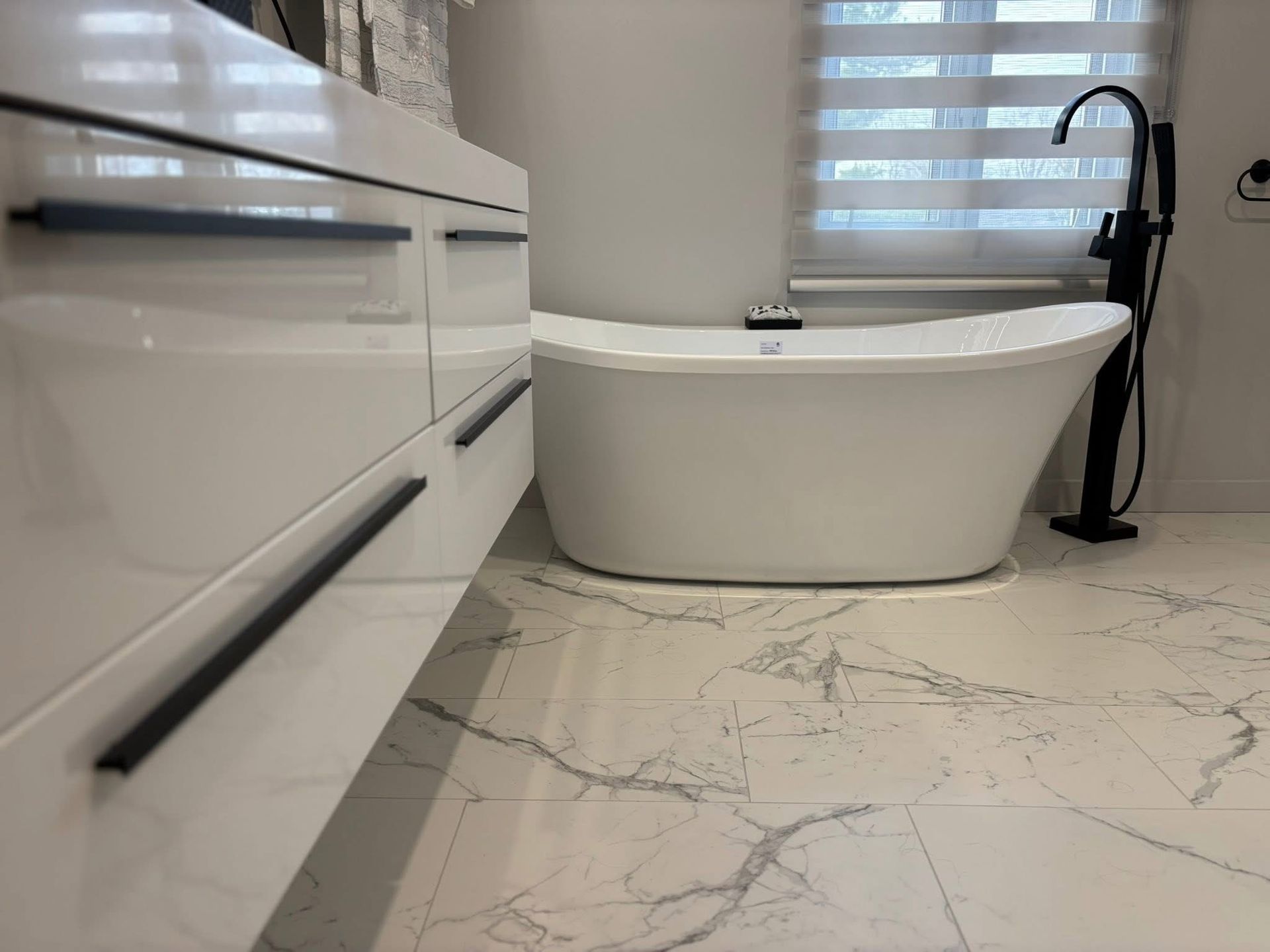 Salle de bains moderne blanche avec baignoire îlot, robinet noir et carrelage imitation marbre.