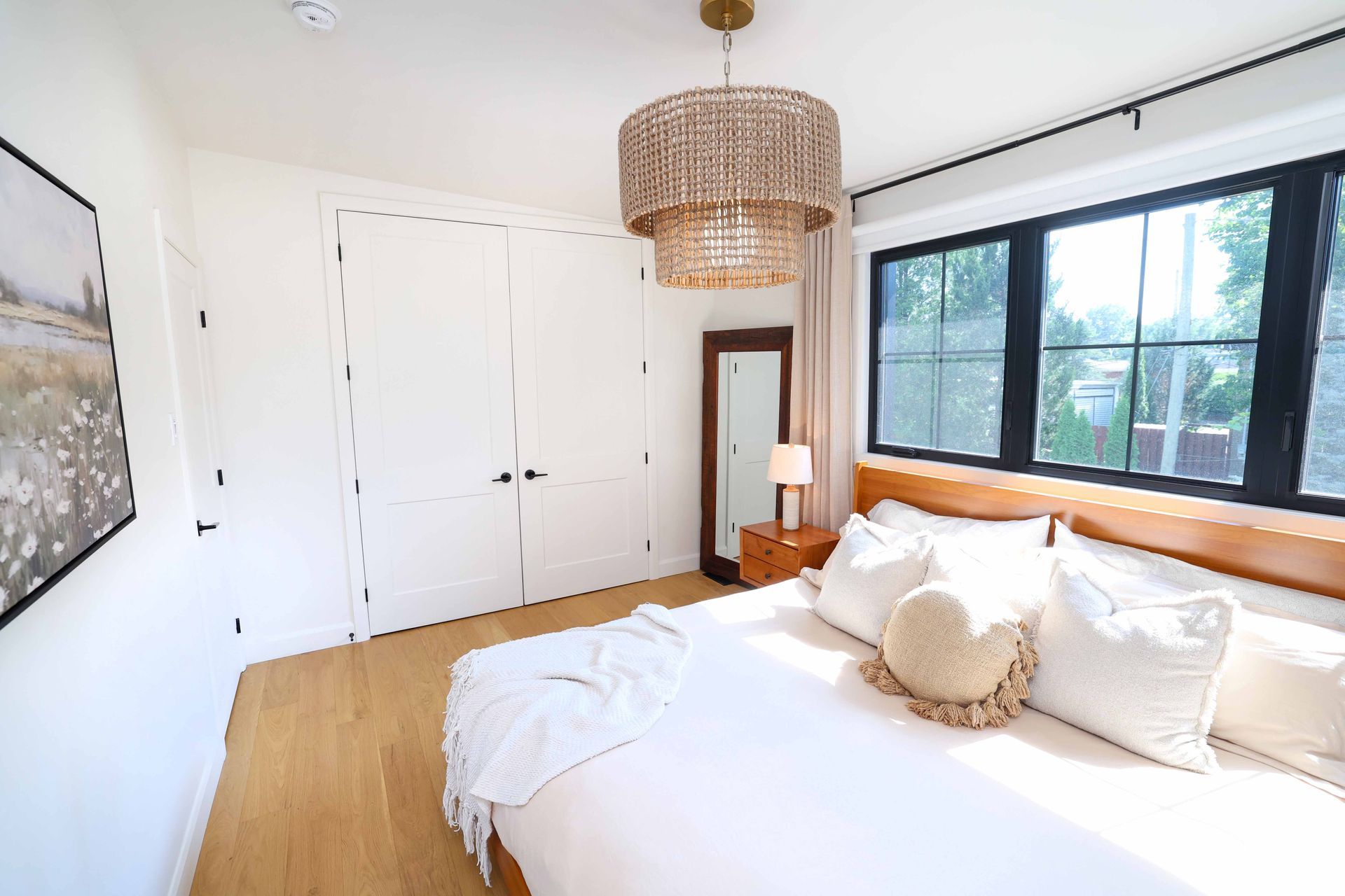 Chambre avec murs blancs, portes de placard et lit blancs. Parquet, fenêtres à cadre noir et lustre décoratif.