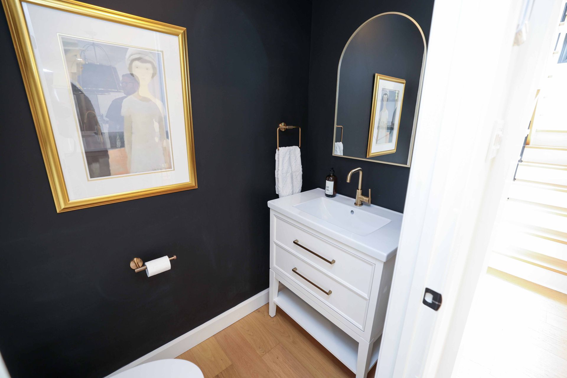 Petite salle de bains aux murs sombres, avec meuble-lavabo blanc, robinetterie dorée et œuvres d'art encadrées.