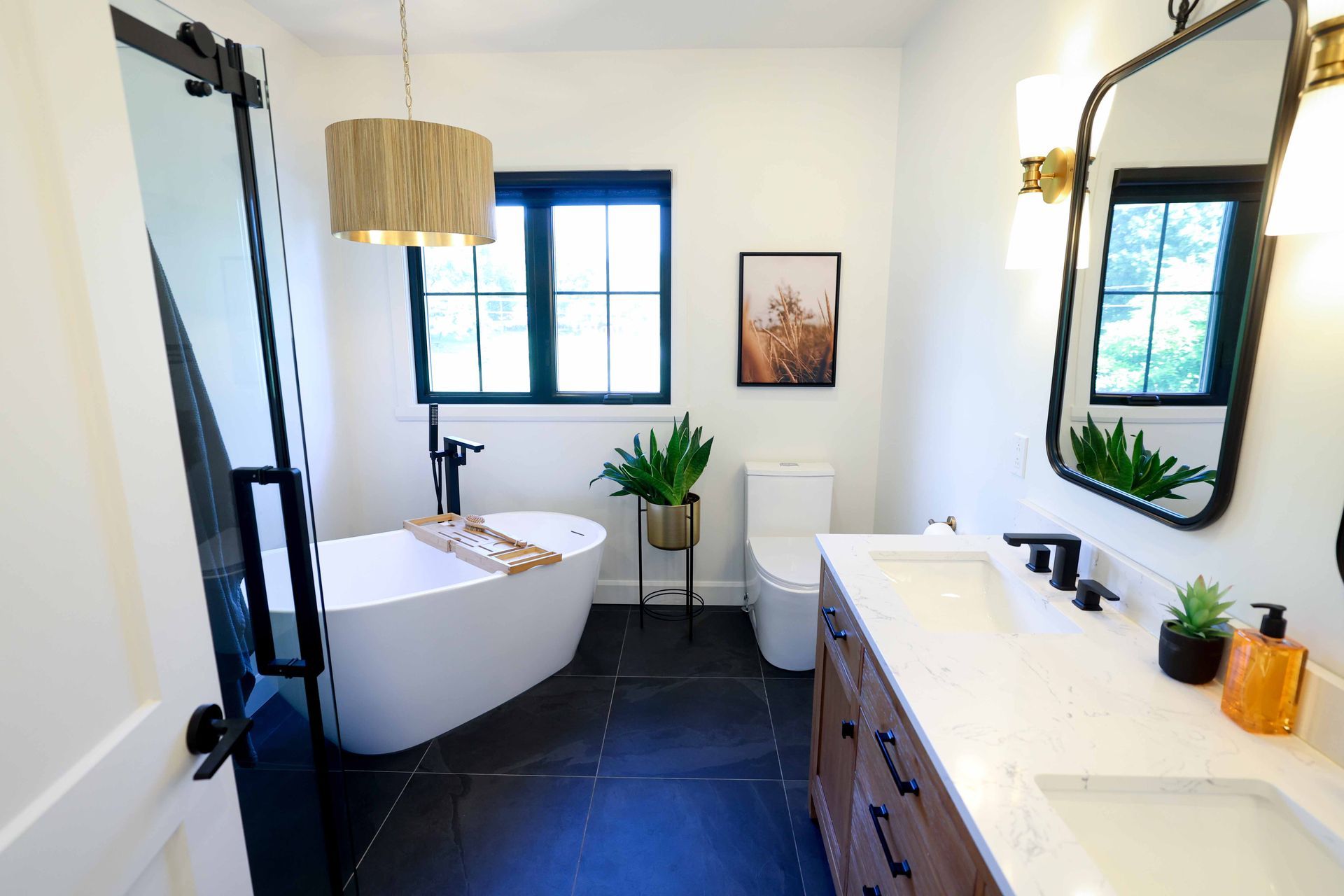 Salle de bains moderne avec baignoire îlot, sol carrelé foncé et double vasque.