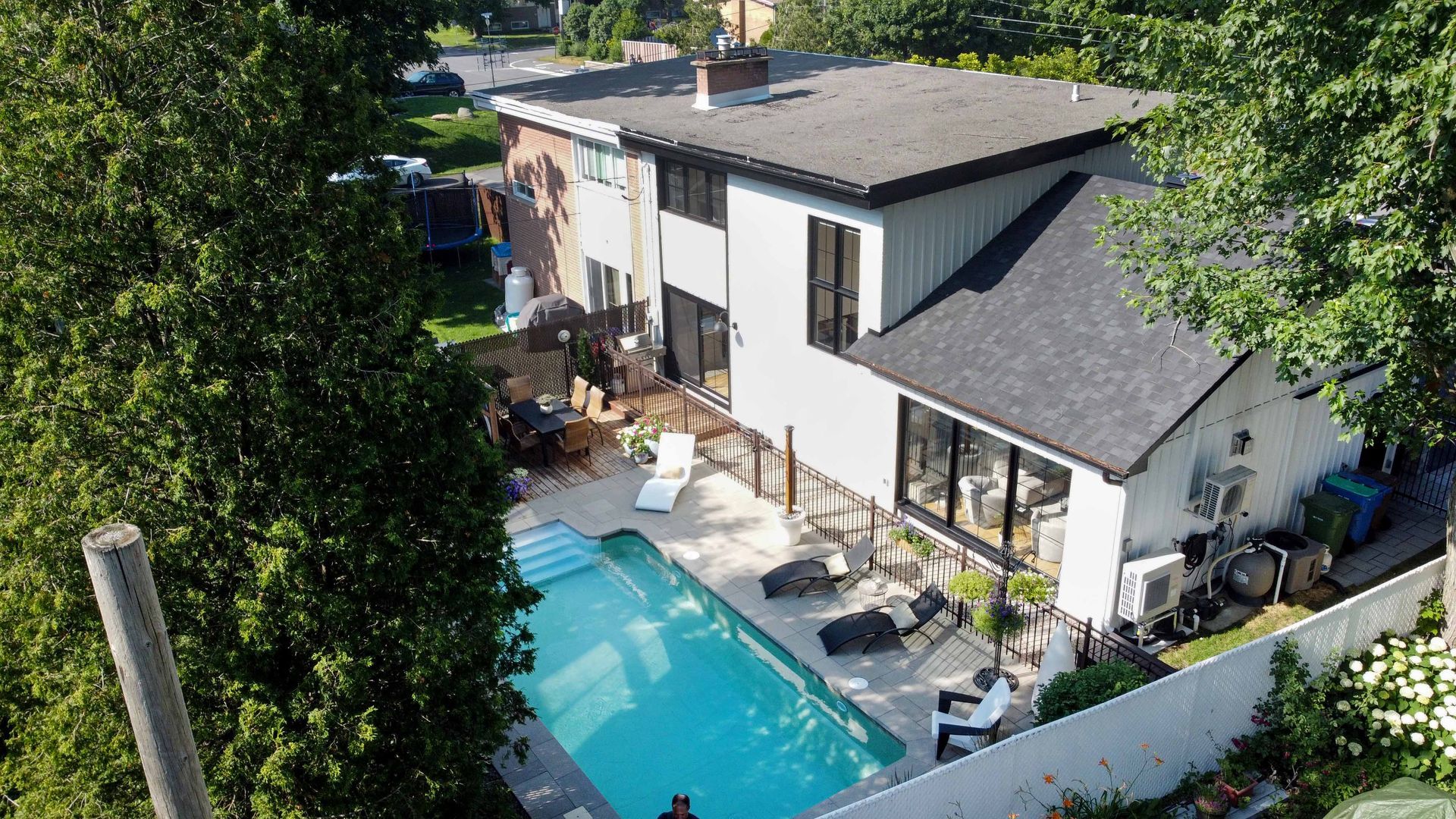 Maison à deux étages avec piscine et coin salon extérieur, vue d'en haut, entourée d'arbres.