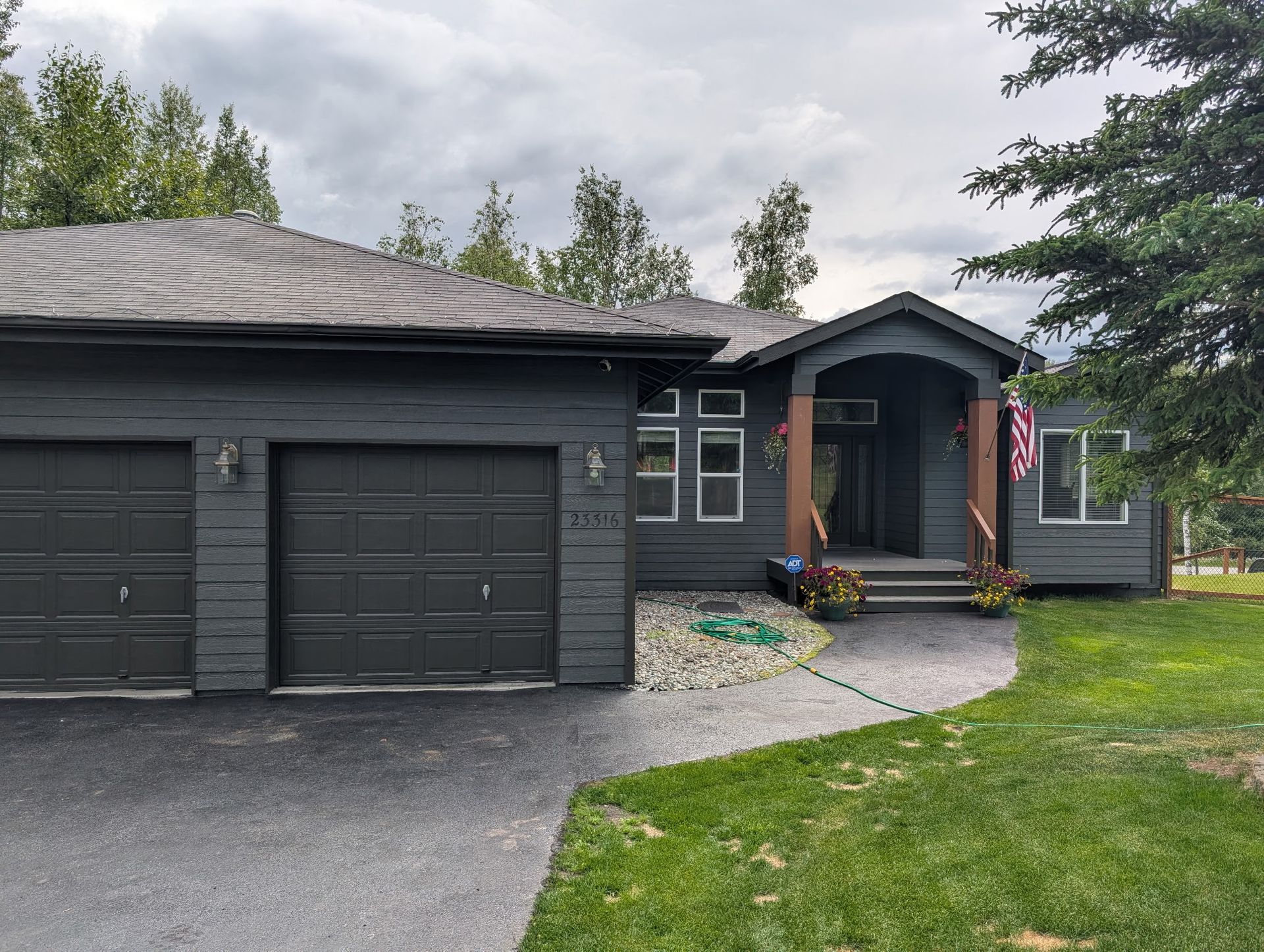 Dark gray suburban house with two garage doors, front porch, and curved walkway on a green lawn.