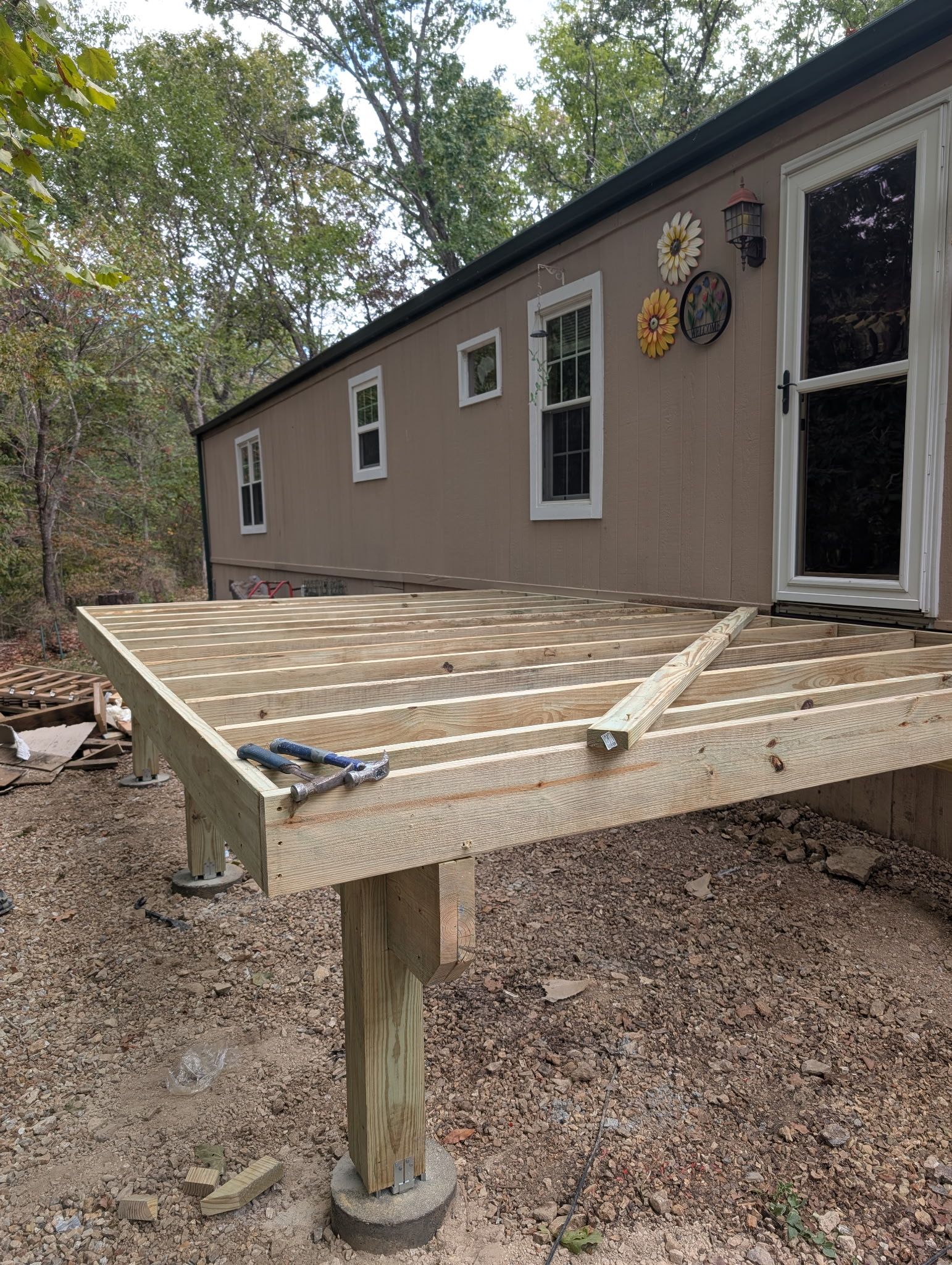 Partially built wooden deck attached to a brown house in a wooded area