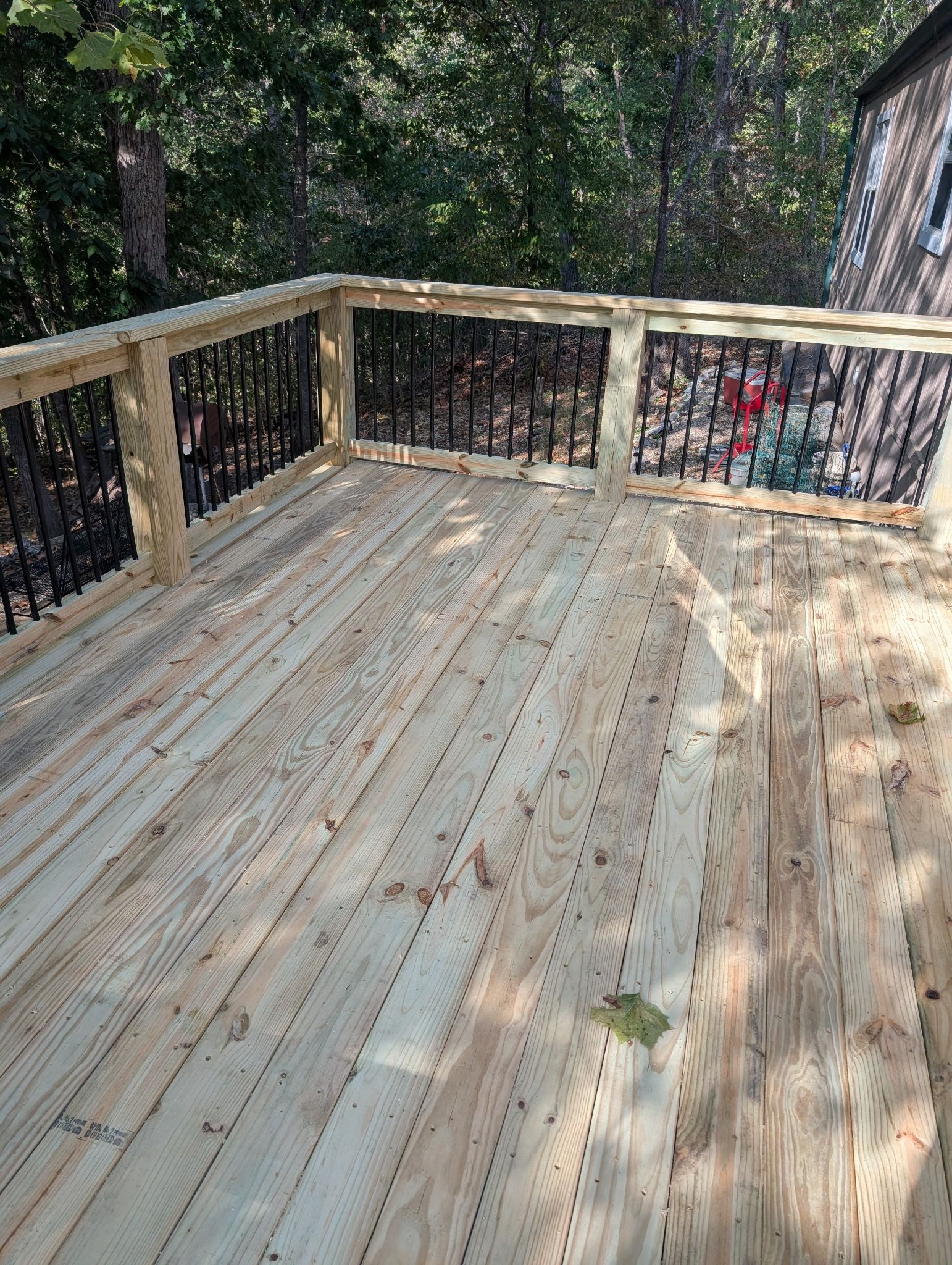 Wooden deck with railing and forest trees beyond, sunlit with dappled shadows.