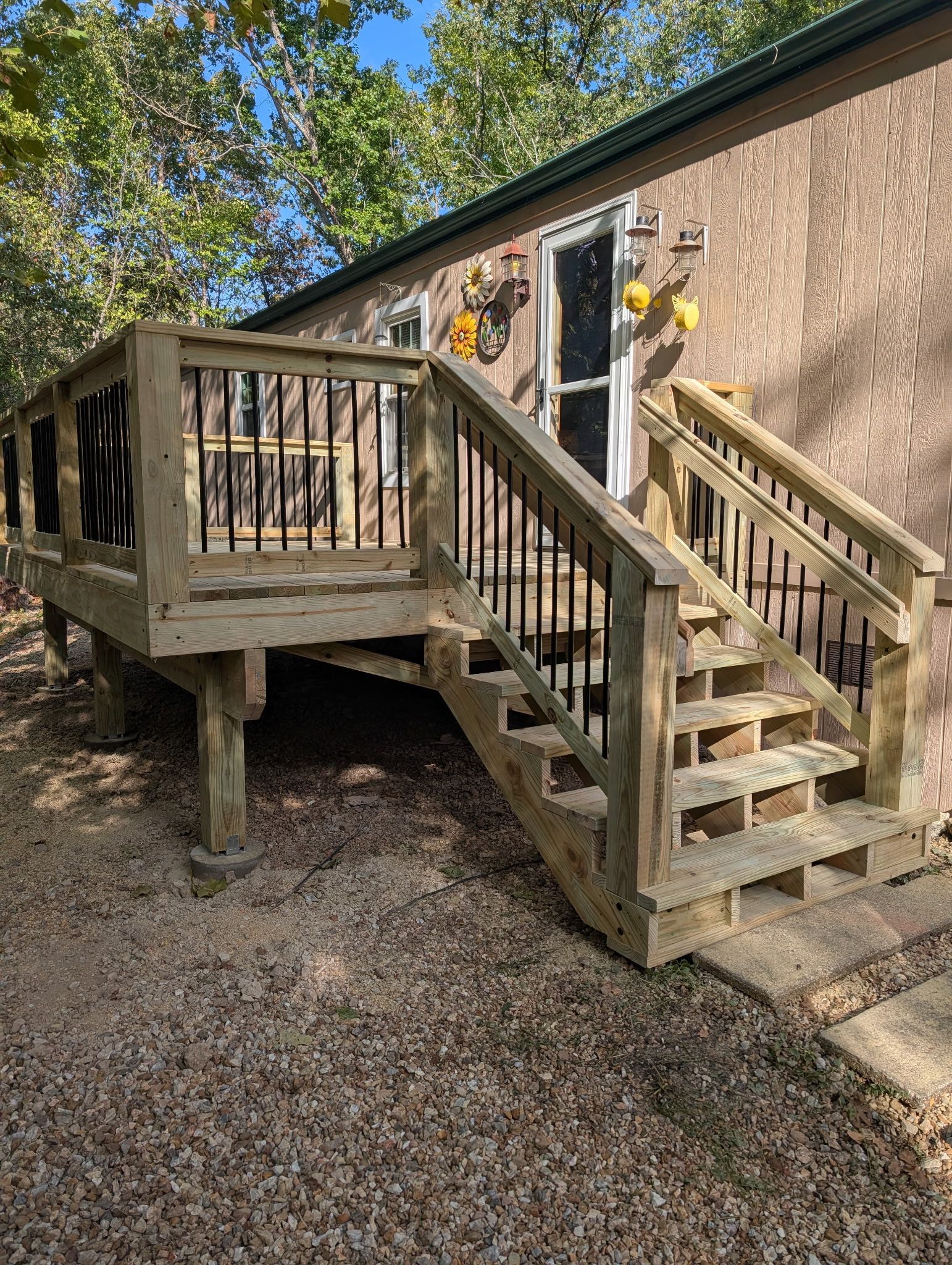 Wooden backyard deck with stairs and railing beside a brick house in a wooded yard