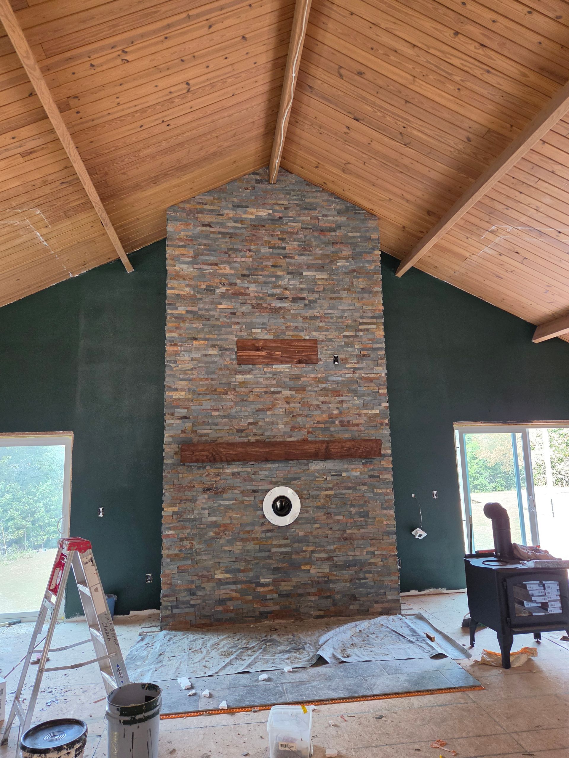 Stone fireplace in a vaulted room with wood ceiling, green walls, and renovation tools on the floor