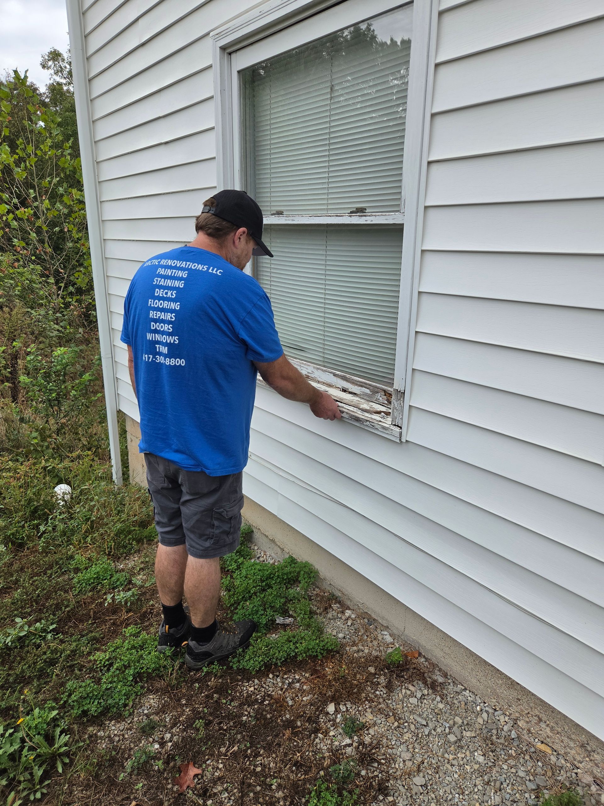Person in blue shirt inspecting a window on the side of a house.