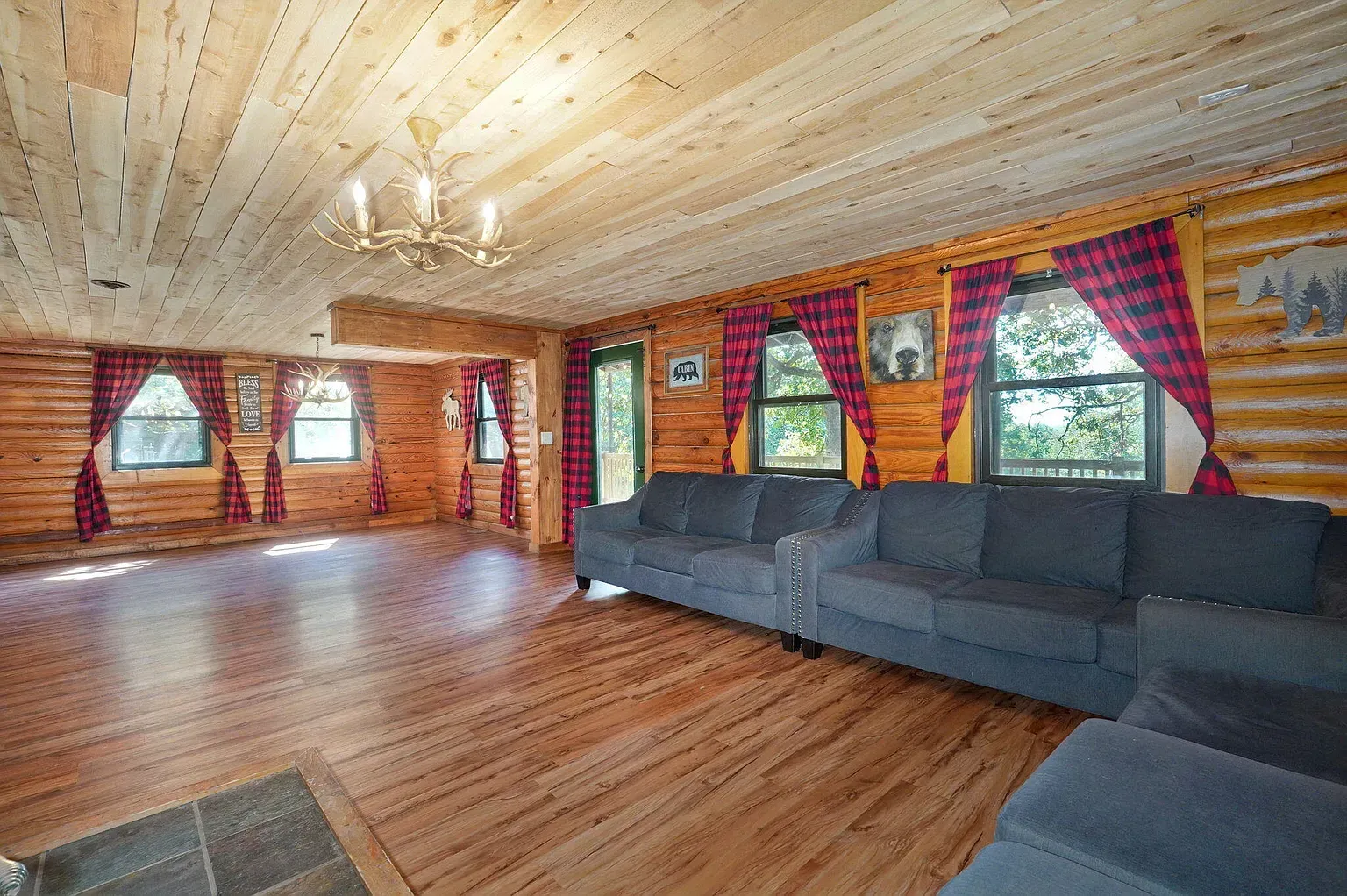 Rustic log cabin living room with wood walls, vaulted ceiling, gray sectional, and colorful curtains
