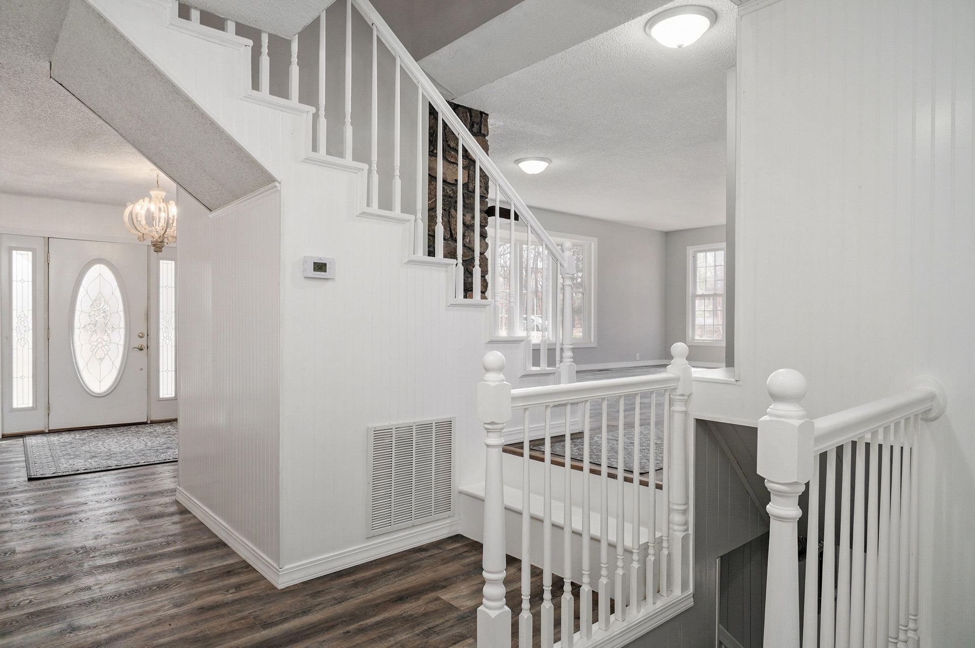 Bright white entryway with staircase, railing, and dark wood floors in a modern home