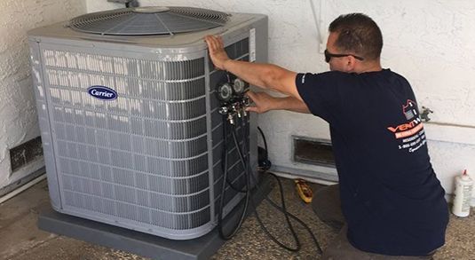A man is working on an air conditioner in a garage.