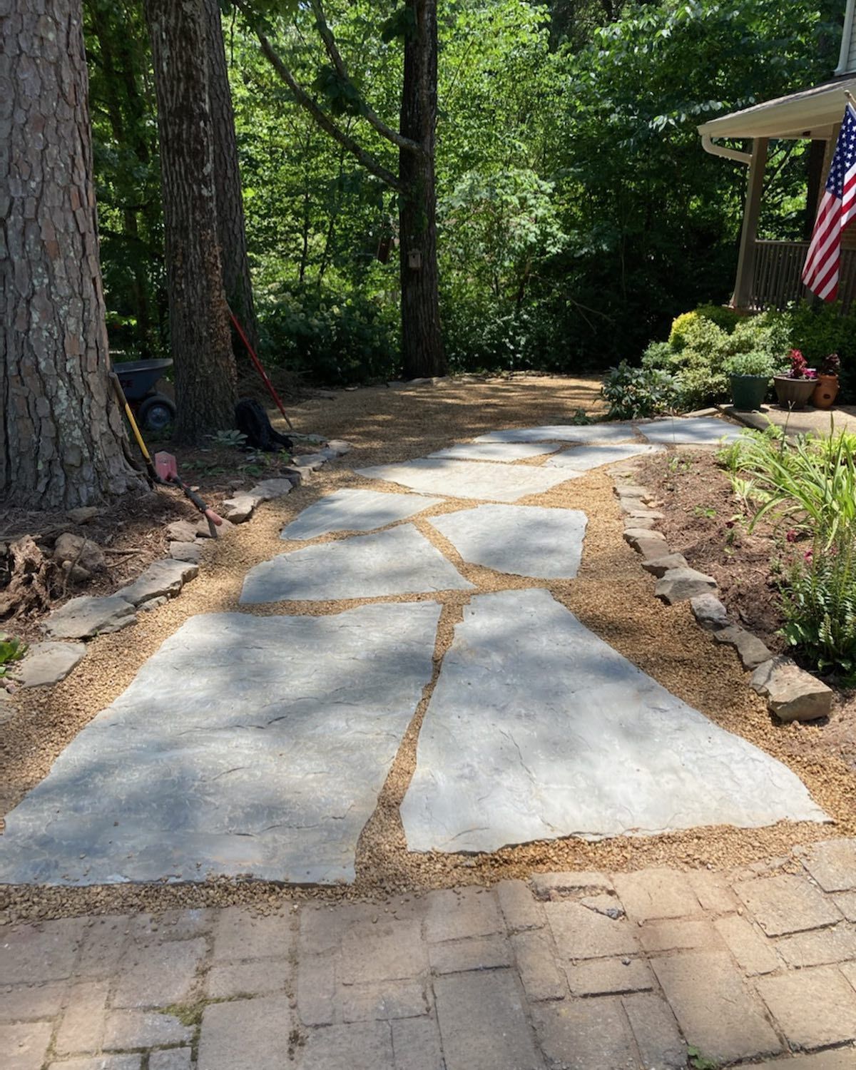 Stone walkway with flagstones bordered by gravel, leading to a house with an American flag.