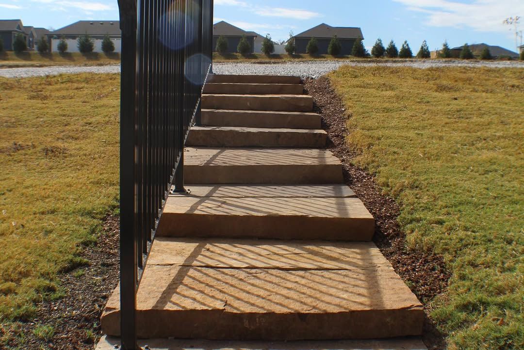 Concrete steps with a black metal railing leading up a slight incline in a grassy yard.