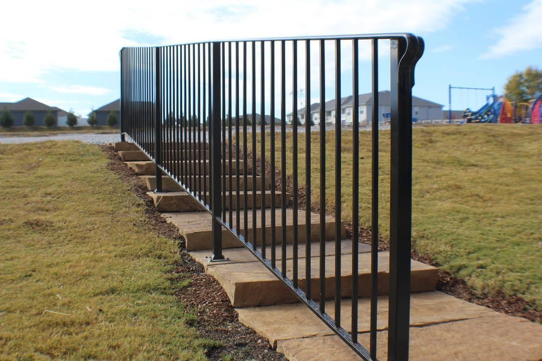 Black metal railing next to stone steps leading up a grassy hill towards a playground.