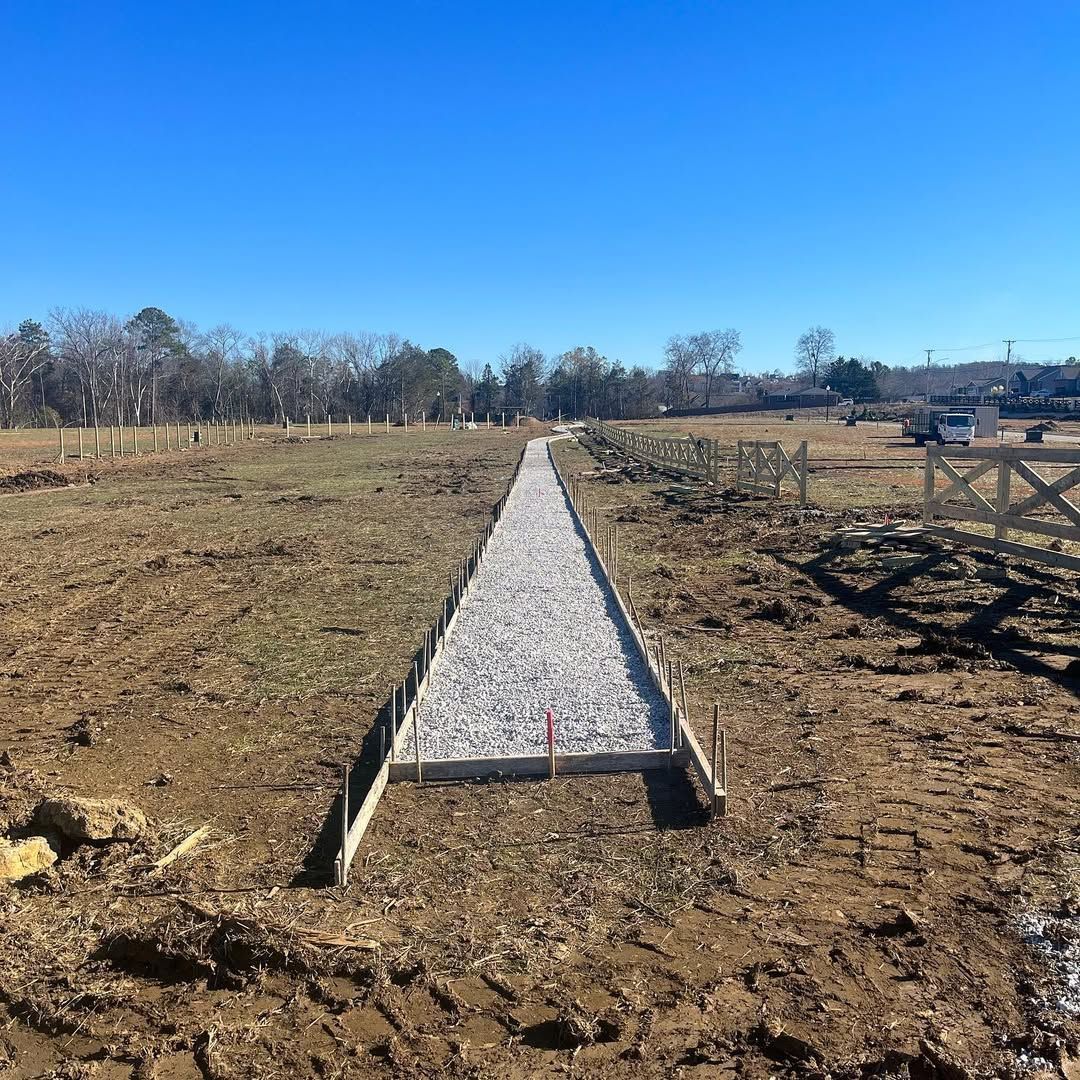 Concrete path under construction in a field, surrounded by dirt and wooden formwork. Blue sky in the background.