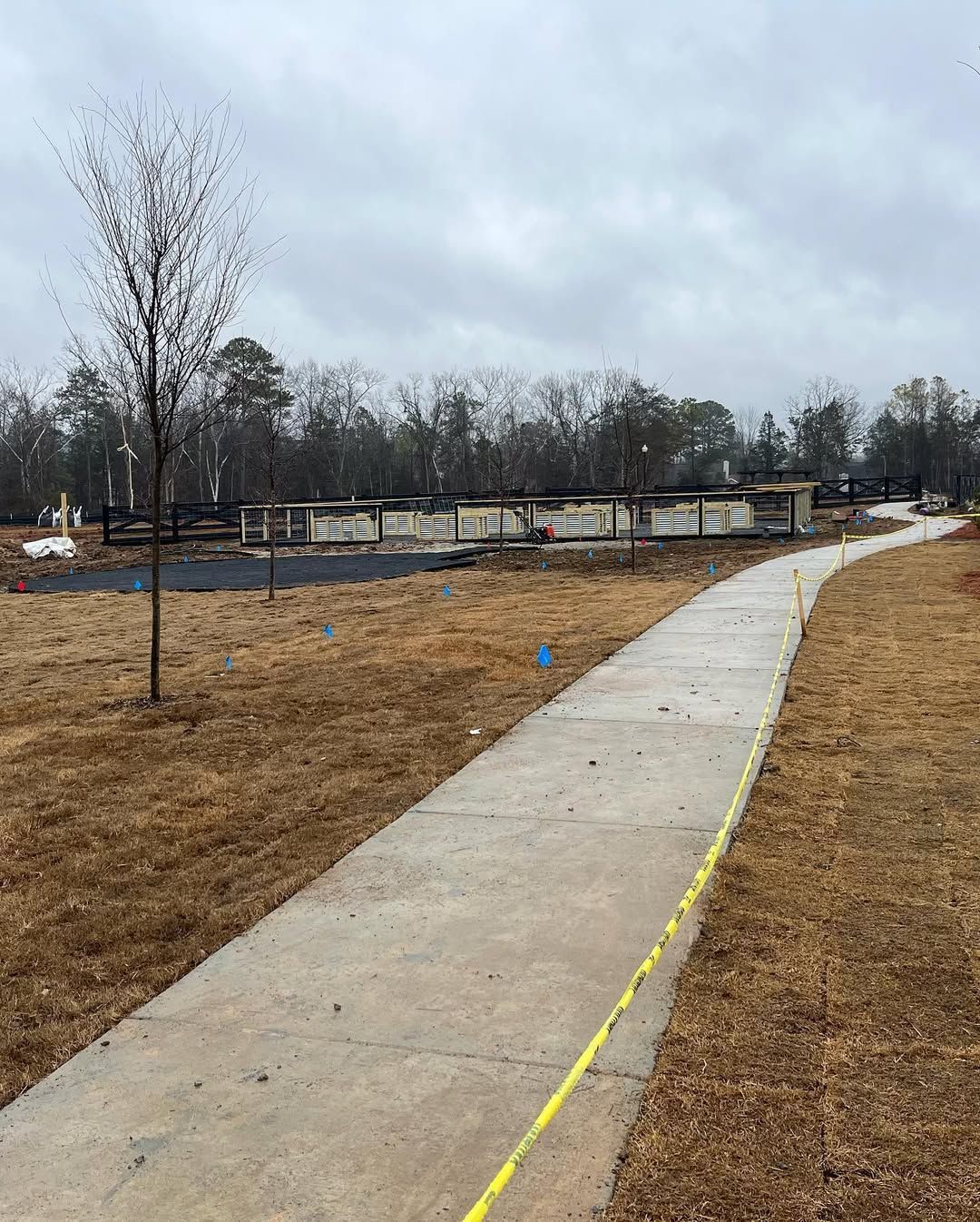 Concrete path through a grassy area, leading toward a dark structure under a cloudy sky.