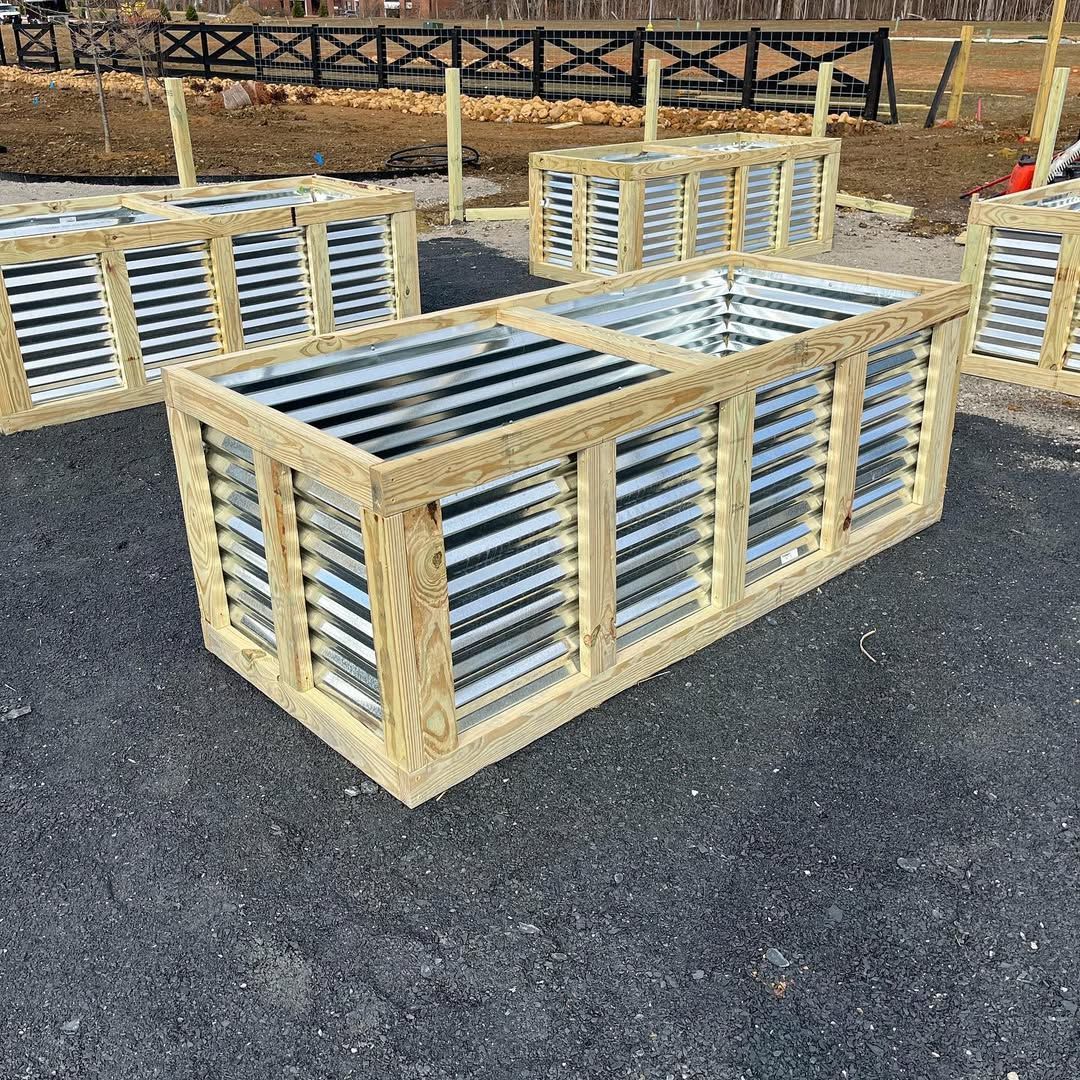 Wooden-framed raised garden beds with corrugated metal siding, outdoors on asphalt.