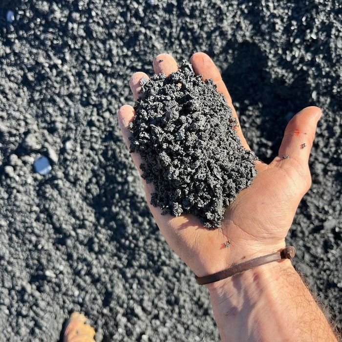 Hand holding a mound of dark gray, granular material, likely volcanic sand or ash.