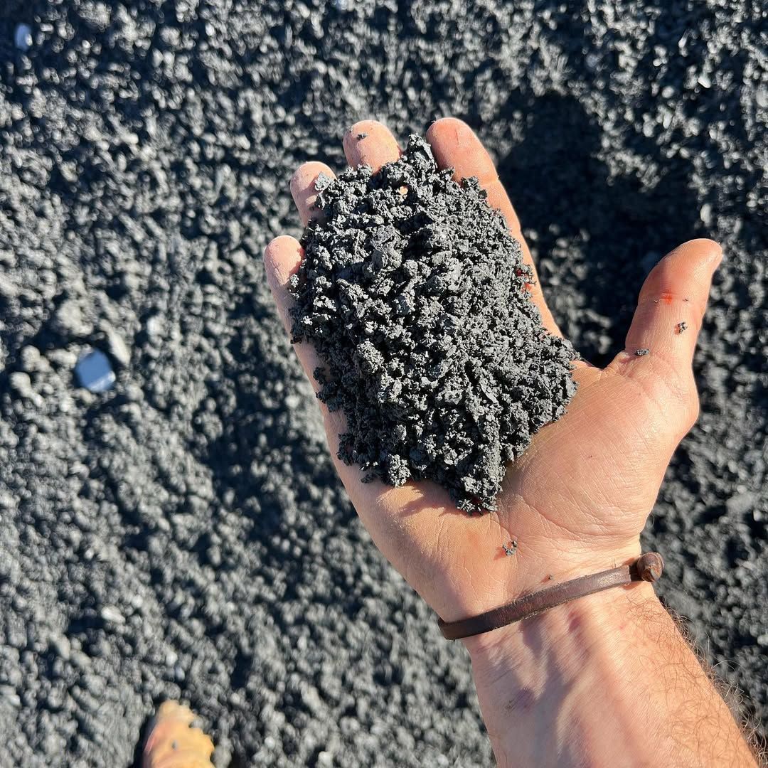 Hand holding a pile of dark, granular material, possibly volcanic sand or ash.