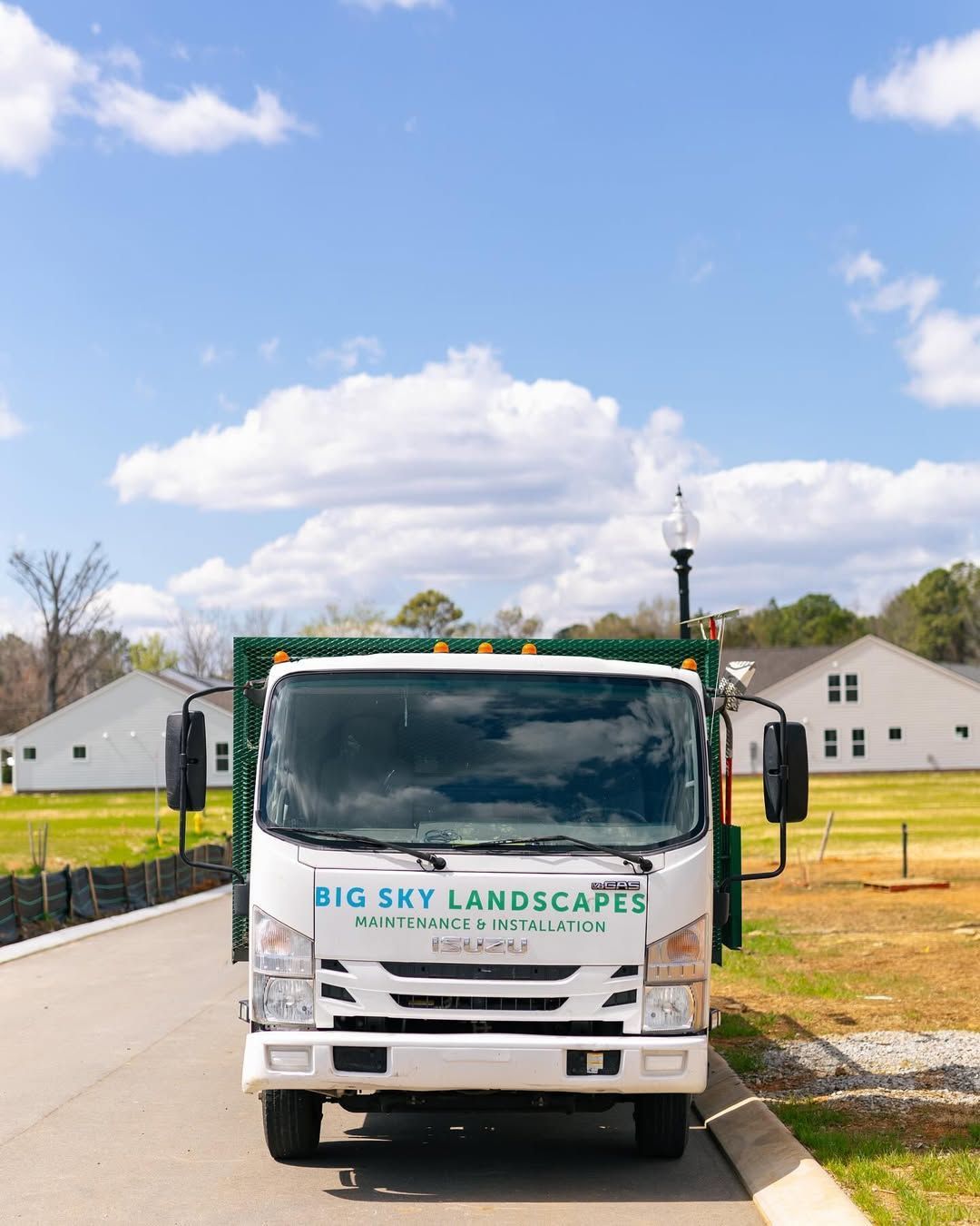White Big Sky Landscaping truck parked on a paved road, in front of a blue sky and white houses.
