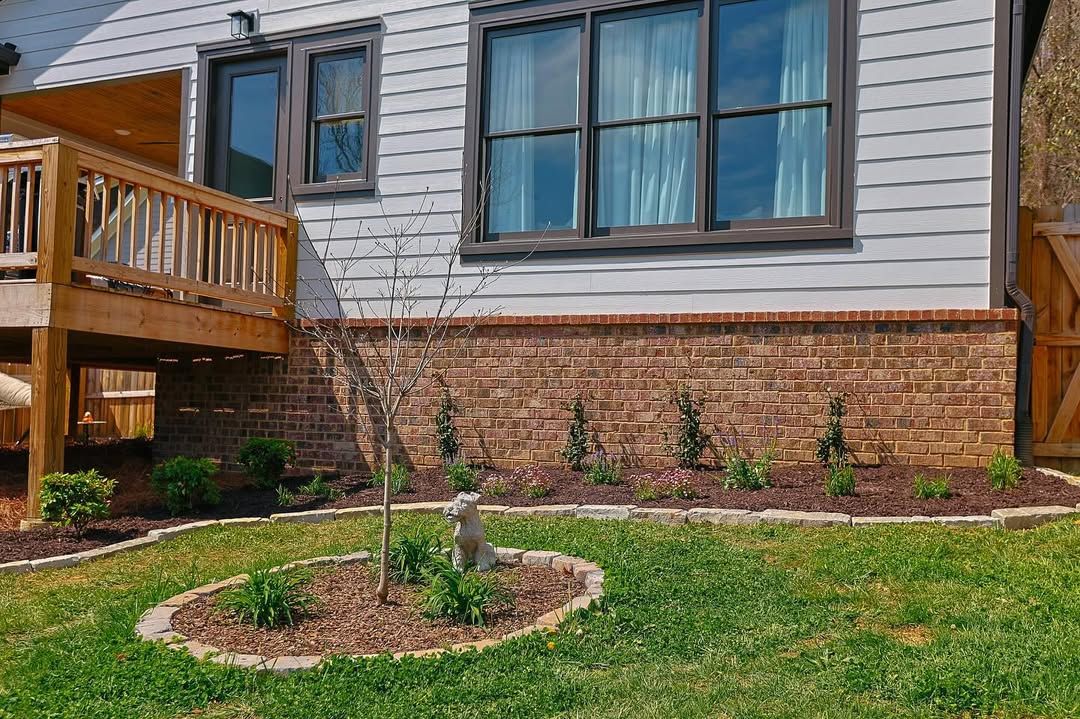 Exterior of a house with a brick foundation, deck, and green lawn with small trees.
