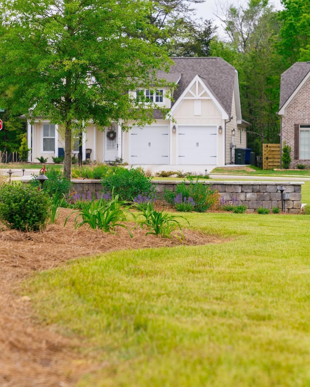 Beige house with two-car garage, green lawn, and a small garden wall.
