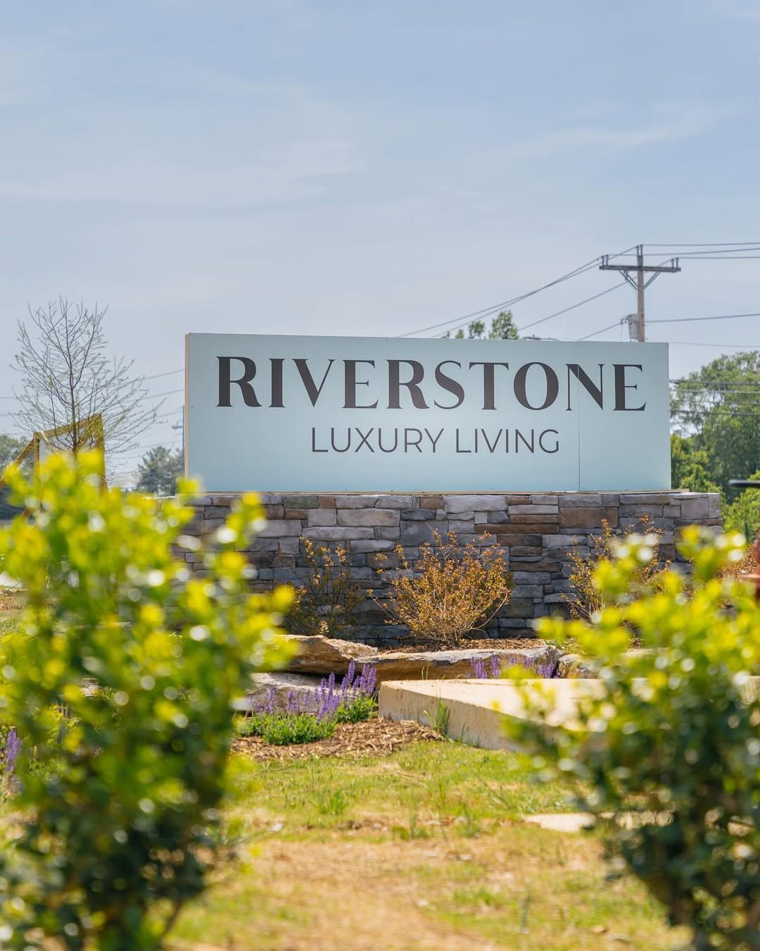 Sign for Riverstone Luxury Living, light blue letters on a white background, atop a stone base.