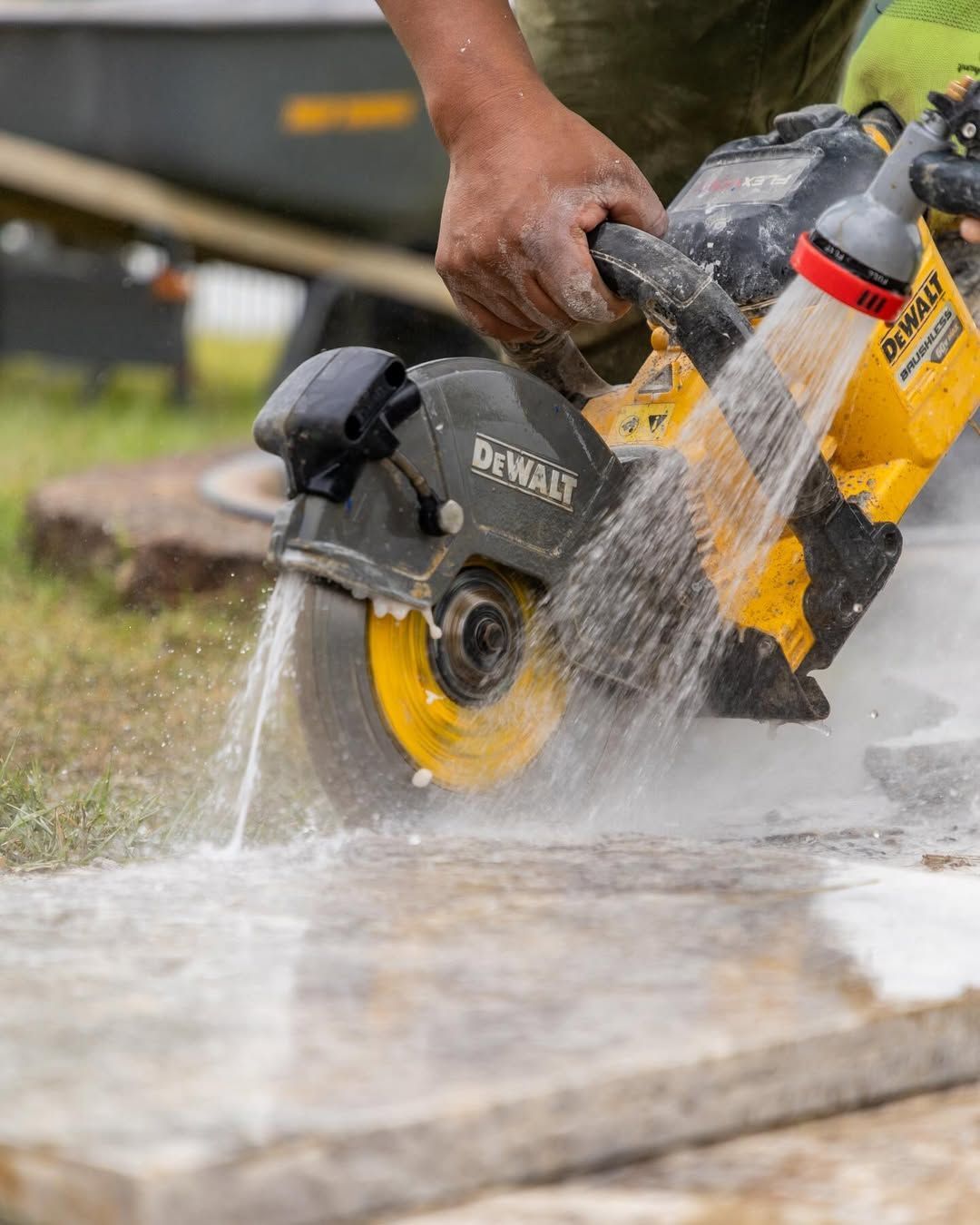 Person using a DeWalt circular saw to cut a stone slab. Water sprays to control dust.