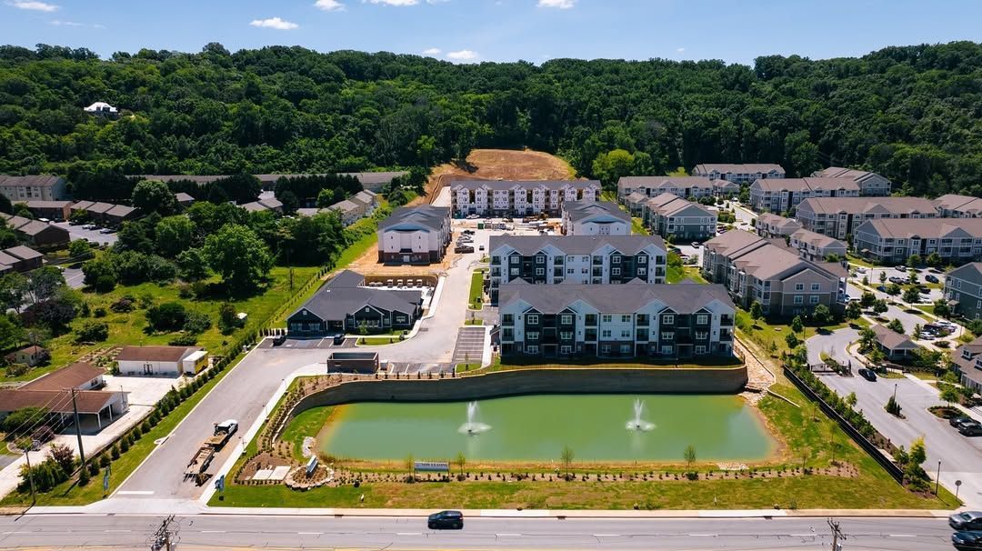 Aerial view of apartment complex with a pond and wooded background.