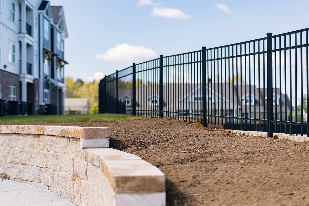 Black metal fence on a low retaining wall; apartments and sky in the background.