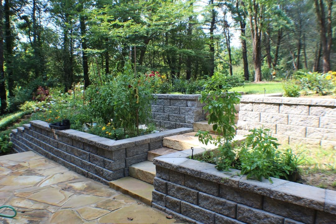 Stone retaining walls with plants and steps, leading to a garden area in a wooded setting.