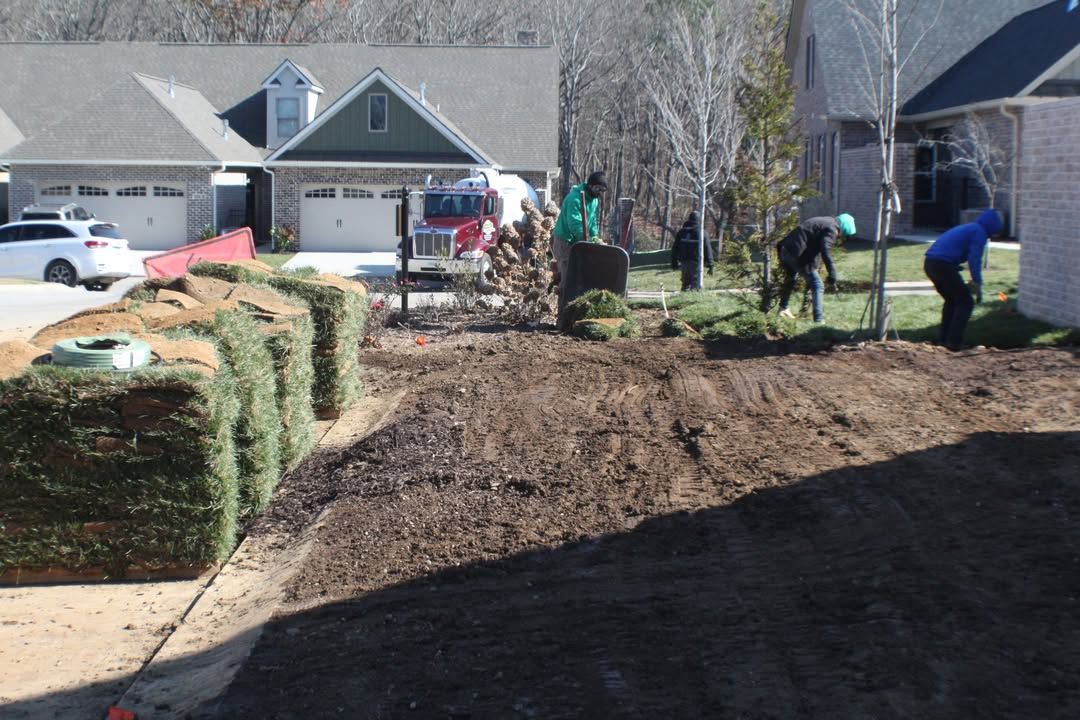 Workers laying sod in front yard of a house. Turf rolls stacked on sidewalk.