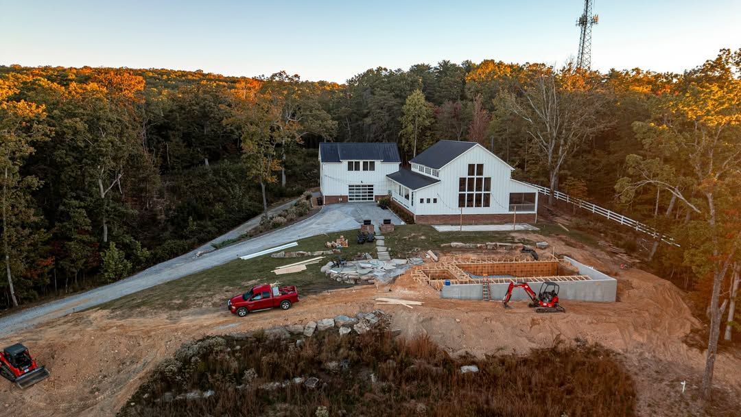 Construction site: white house with pool under construction, red truck, excavators, trees.