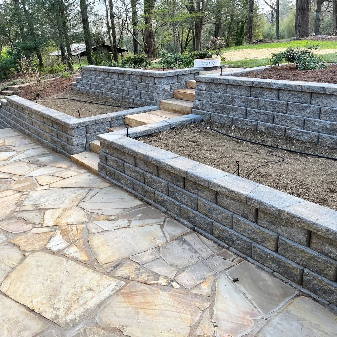 Stone patio with tiered retaining walls, a path, and empty garden beds.