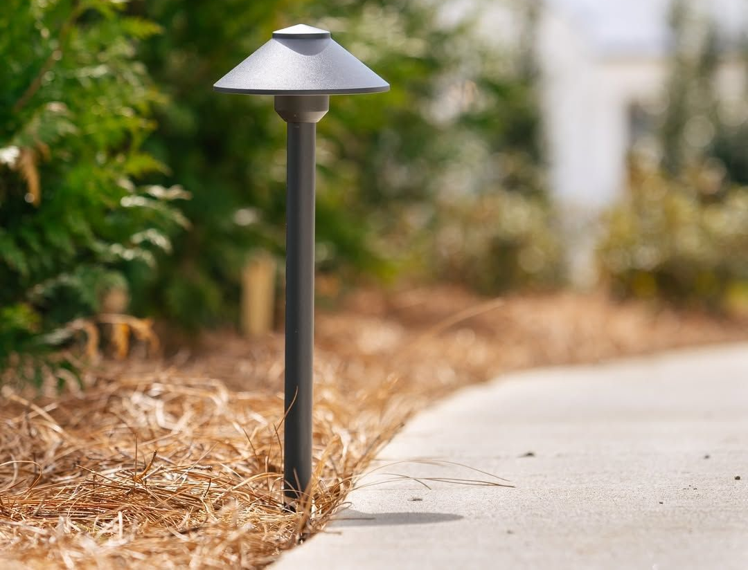 Outdoor path light next to a concrete walkway, green bushes, and brown mulch.