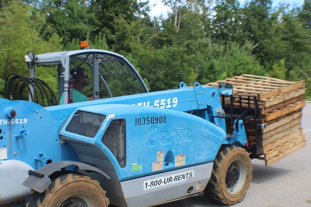 Blue Genie telehandler carrying wooden pallets outdoors.
